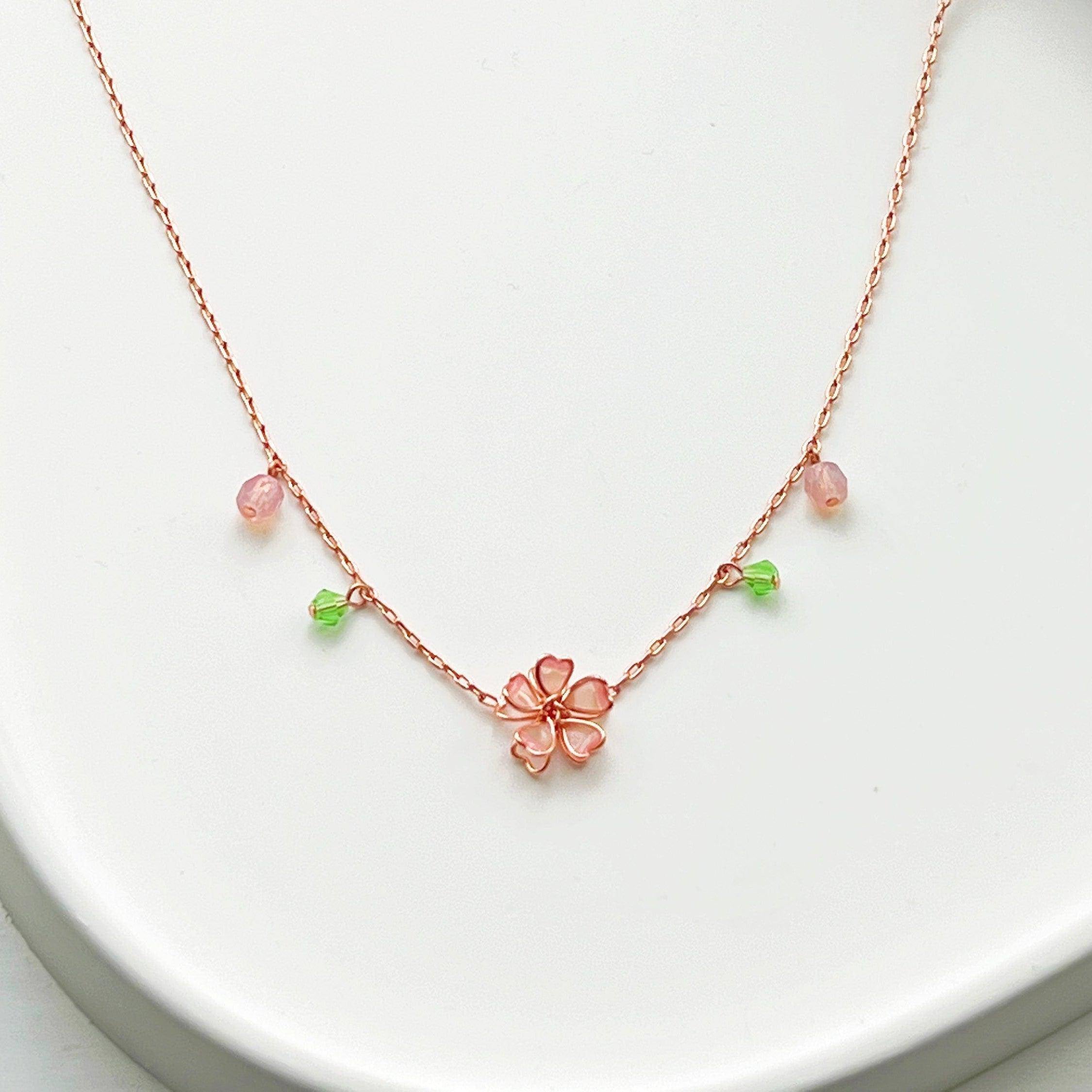 Sakura Flower Necklace featuring pink cherry blossoms and green crystal, handmade with rose gold wire.