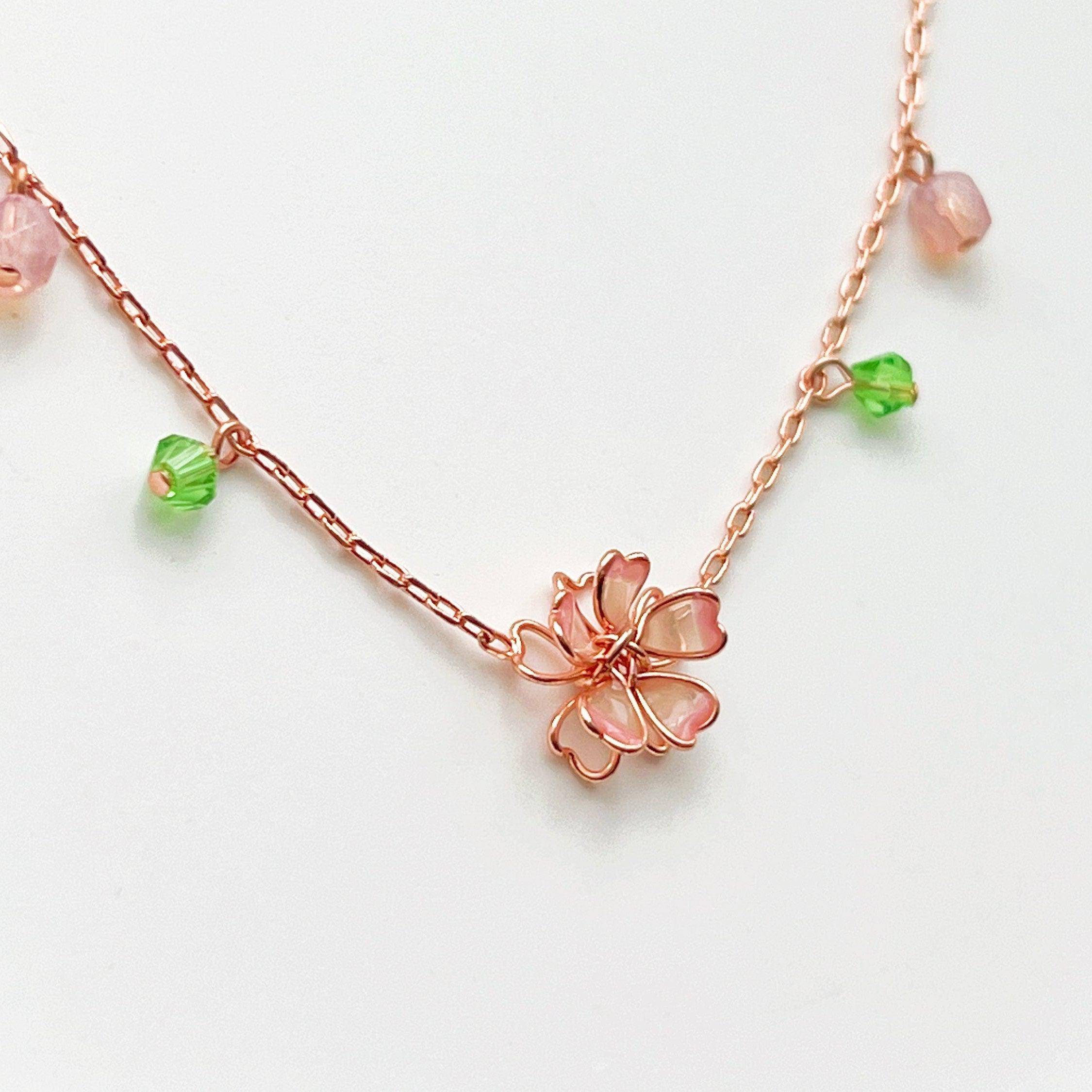 Sakura Flower Necklace featuring pink cherry blossoms and green crystal, handmade with rose gold wire.