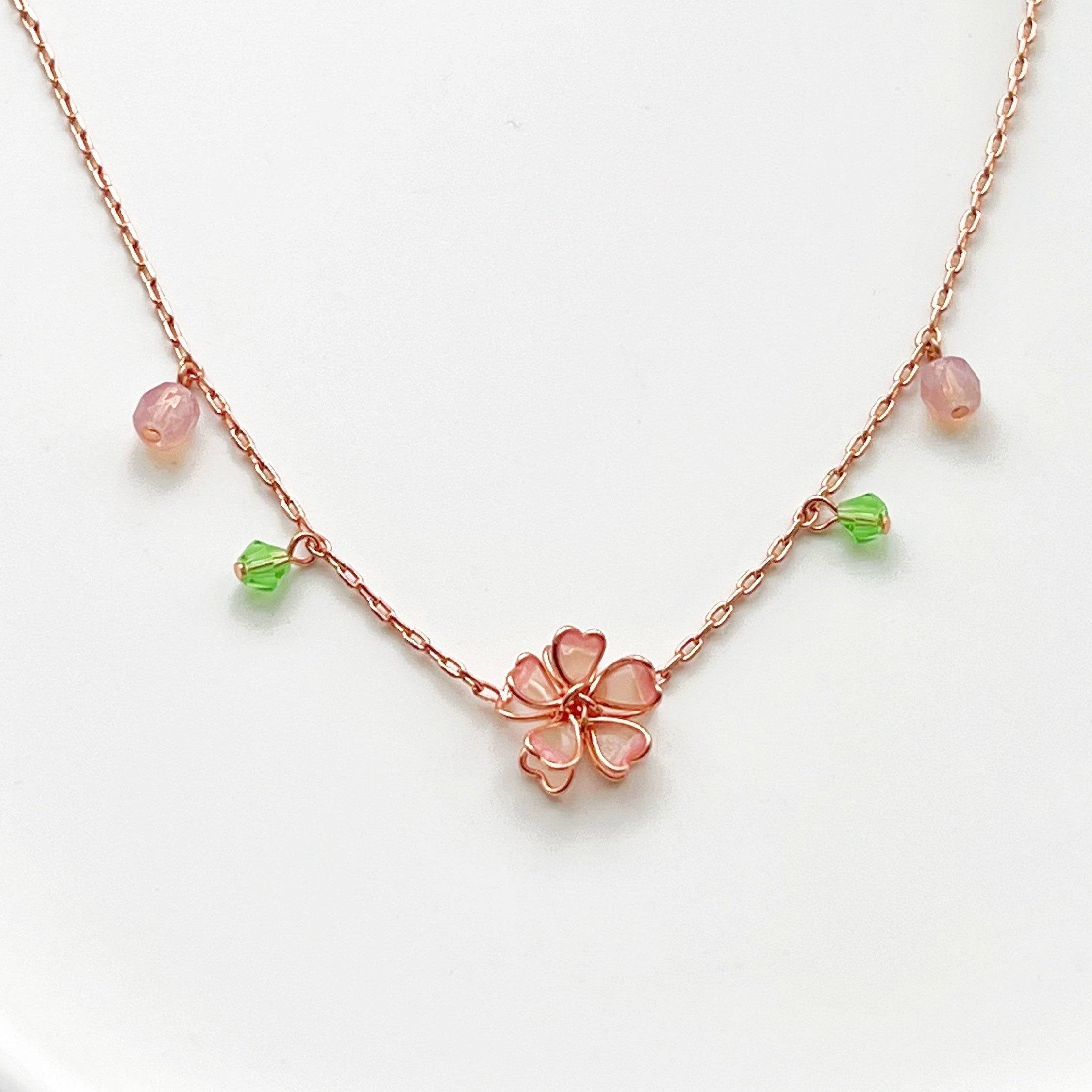 Sakura Flower Necklace featuring pink cherry blossoms and green crystal, handmade with rose gold wire.