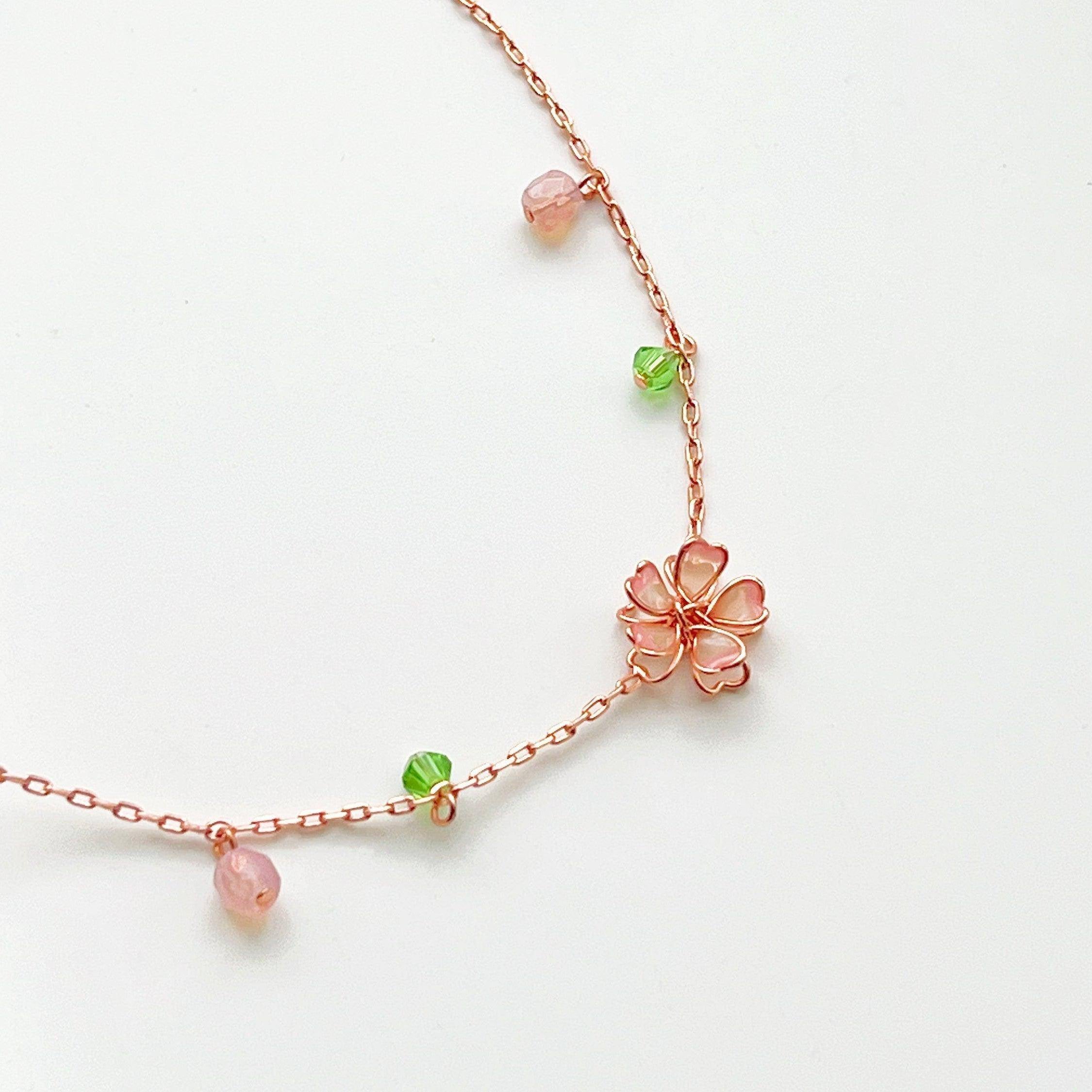 Sakura Flower Necklace featuring pink cherry blossoms and green crystal, handmade with rose gold wire.