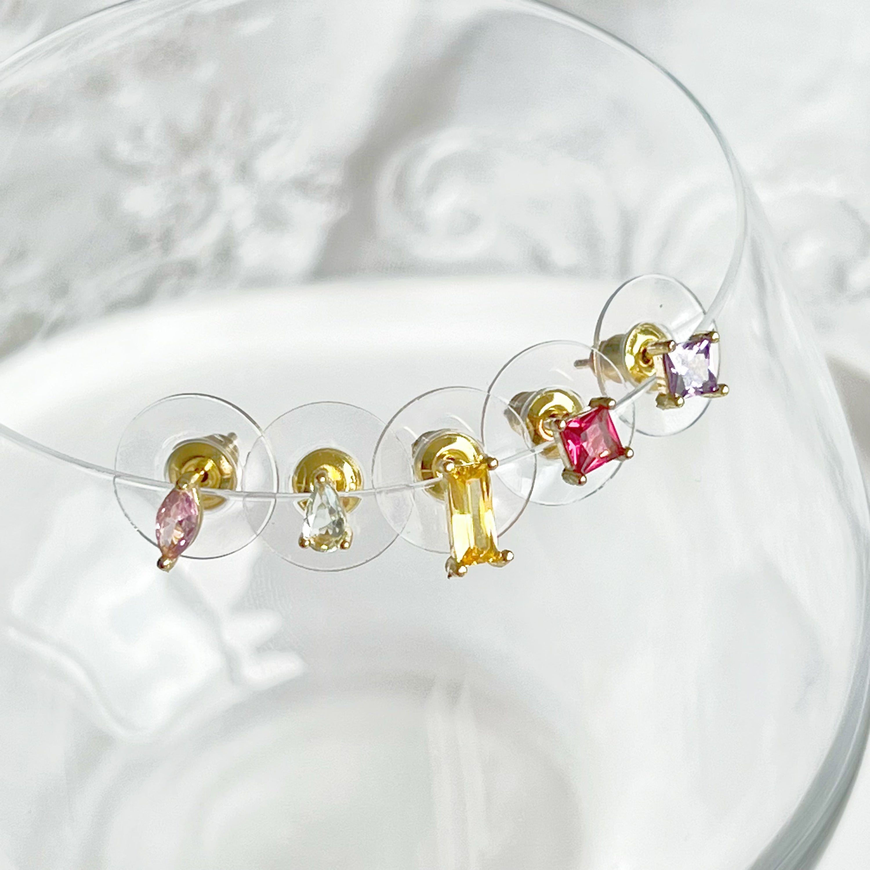 A vibrant set of five rainbow color zircon stud earrings displayed elegantly, showcasing their gold-plated bronze base and sterling silver studs.