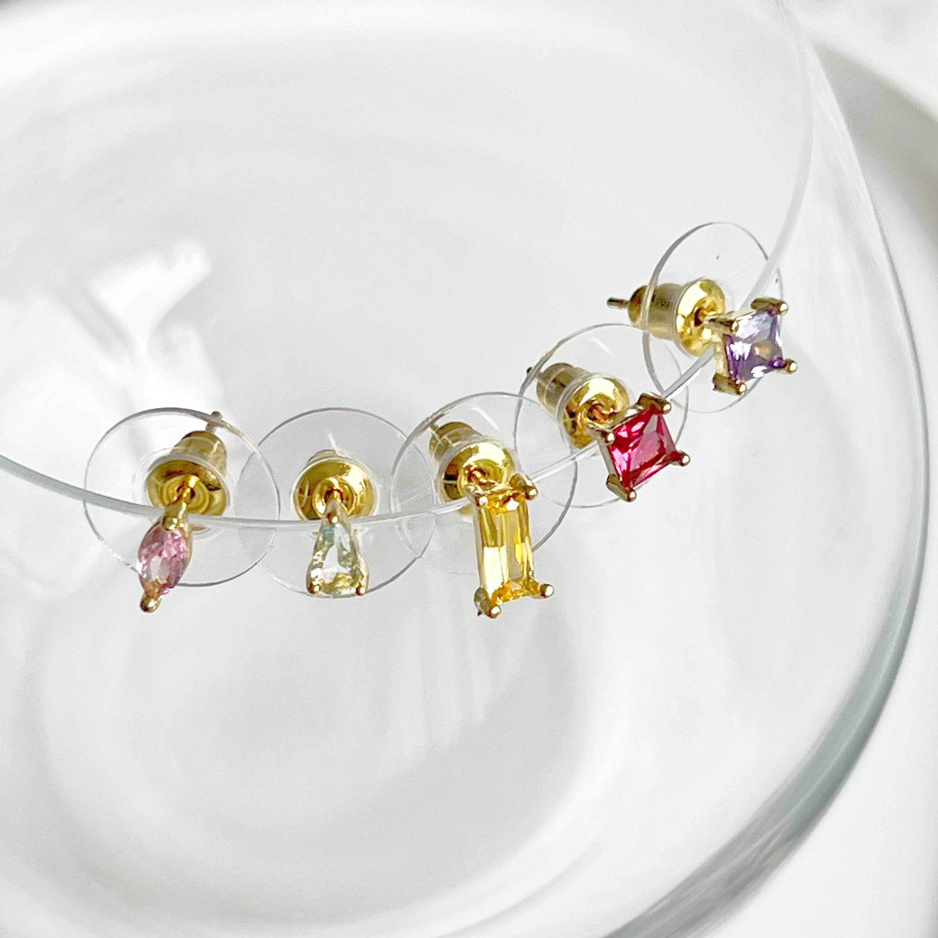 A vibrant set of five rainbow color zircon stud earrings displayed elegantly, showcasing their gold-plated bronze base and sterling silver studs.