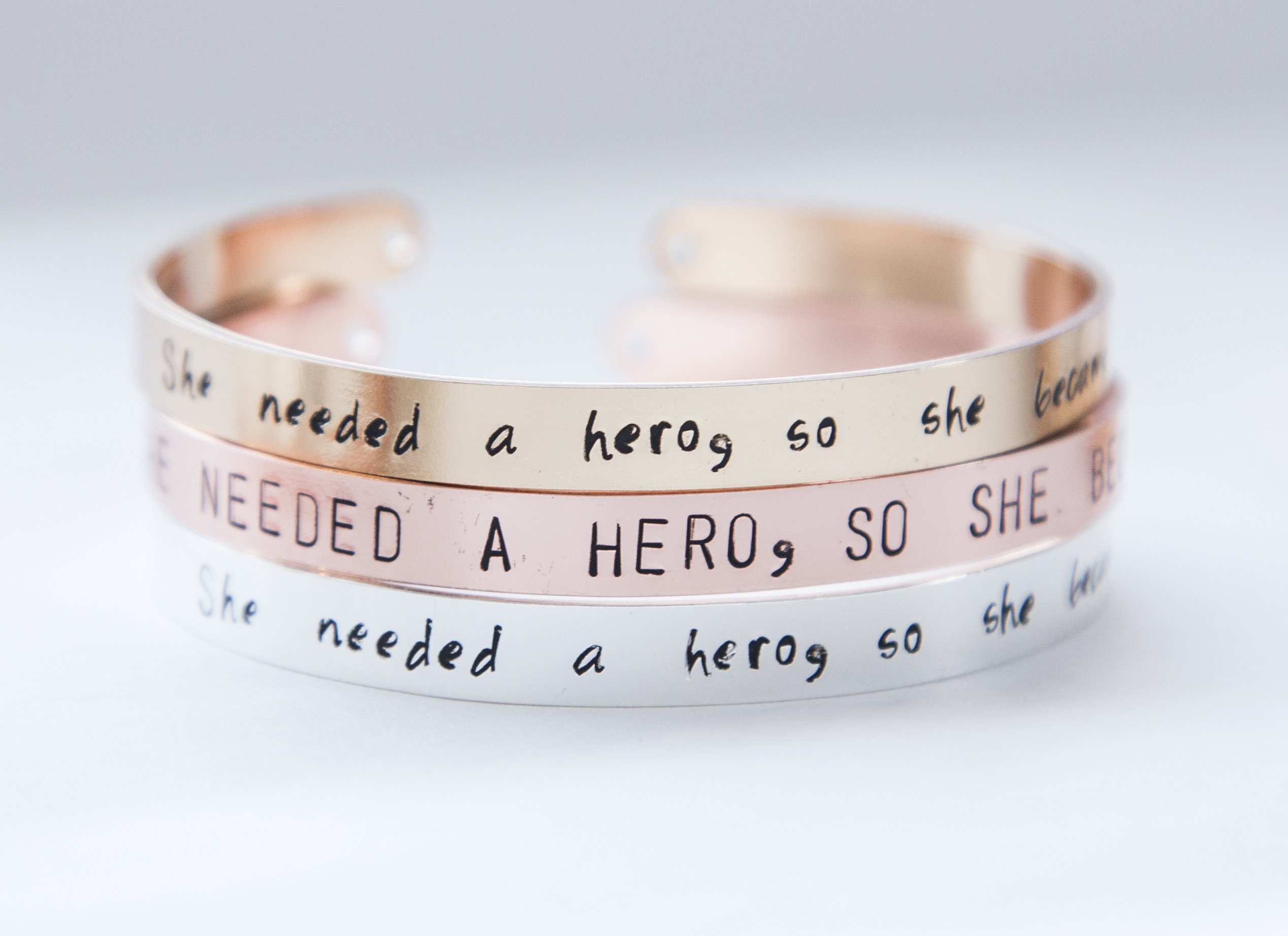 Hand-stamped cuff bracelet in silver, gold, and rose gold plating, showcasing unique lettering and adjustable design.