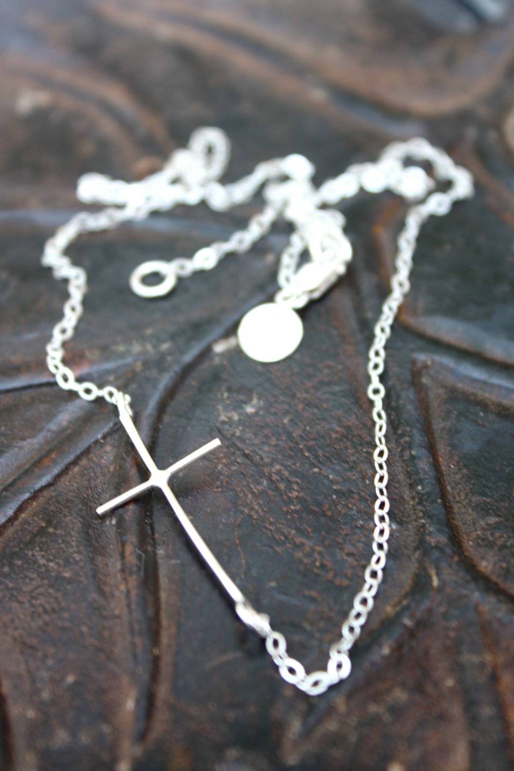 A beautiful sideways cross necklace made from recycled metals, featuring an adjustable chain and a modern design, perfect for special occasions.