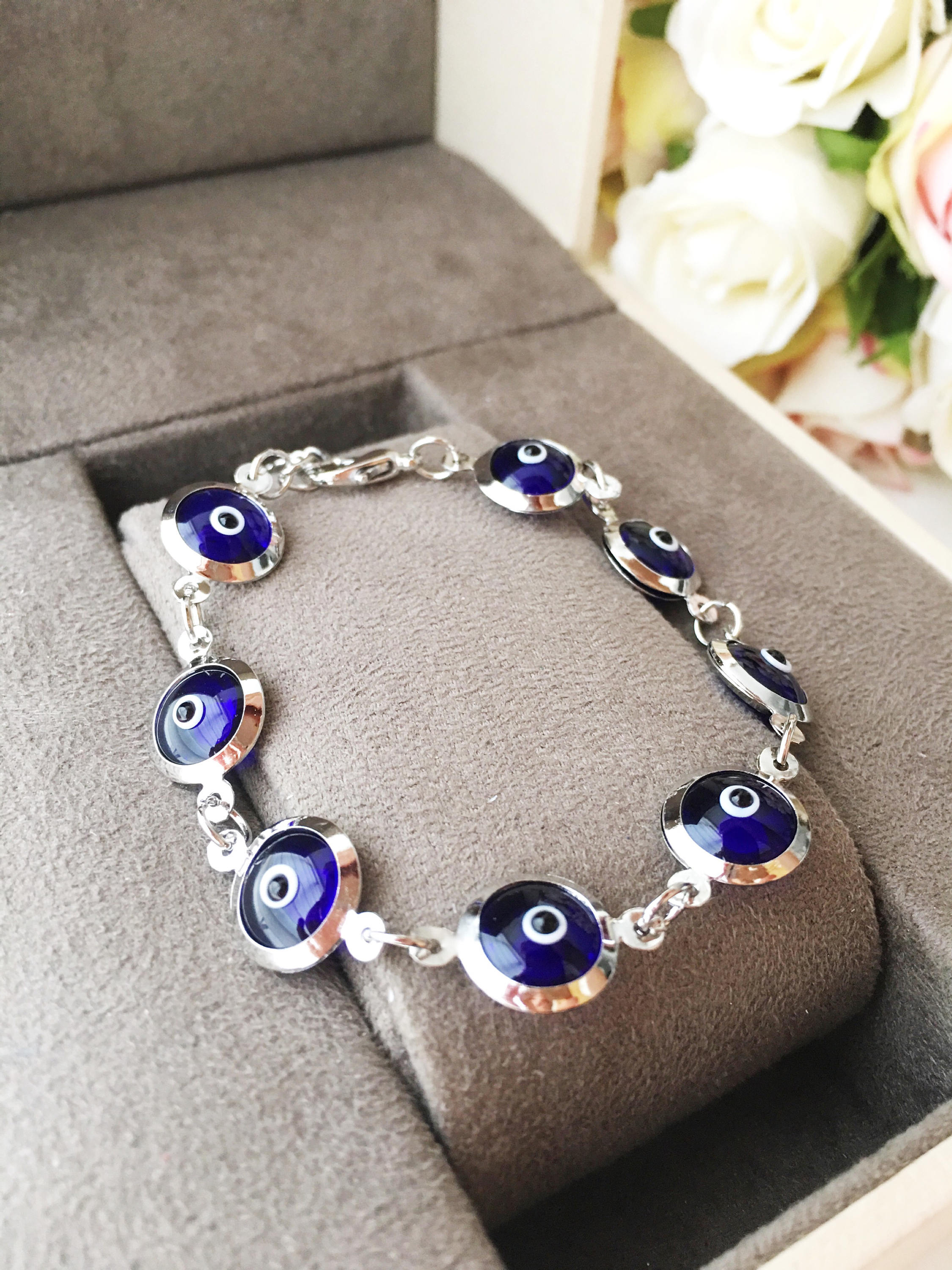 A beautiful silver chain bracelet featuring blue glass evil eye charms, showcasing handmade craftsmanship and elegant design.