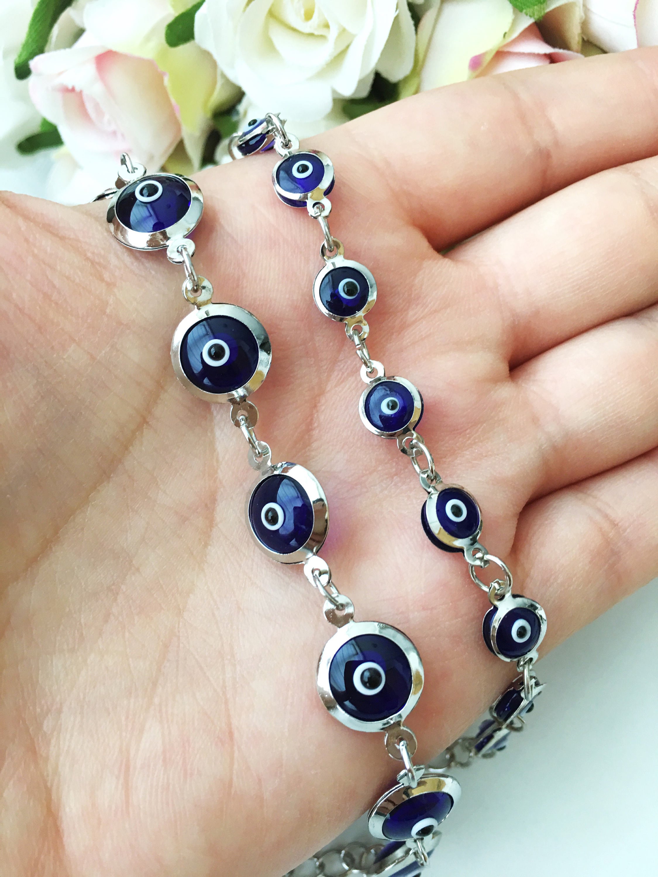 A beautiful silver chain bracelet featuring blue glass evil eye charms, showcasing handmade craftsmanship and elegant design.