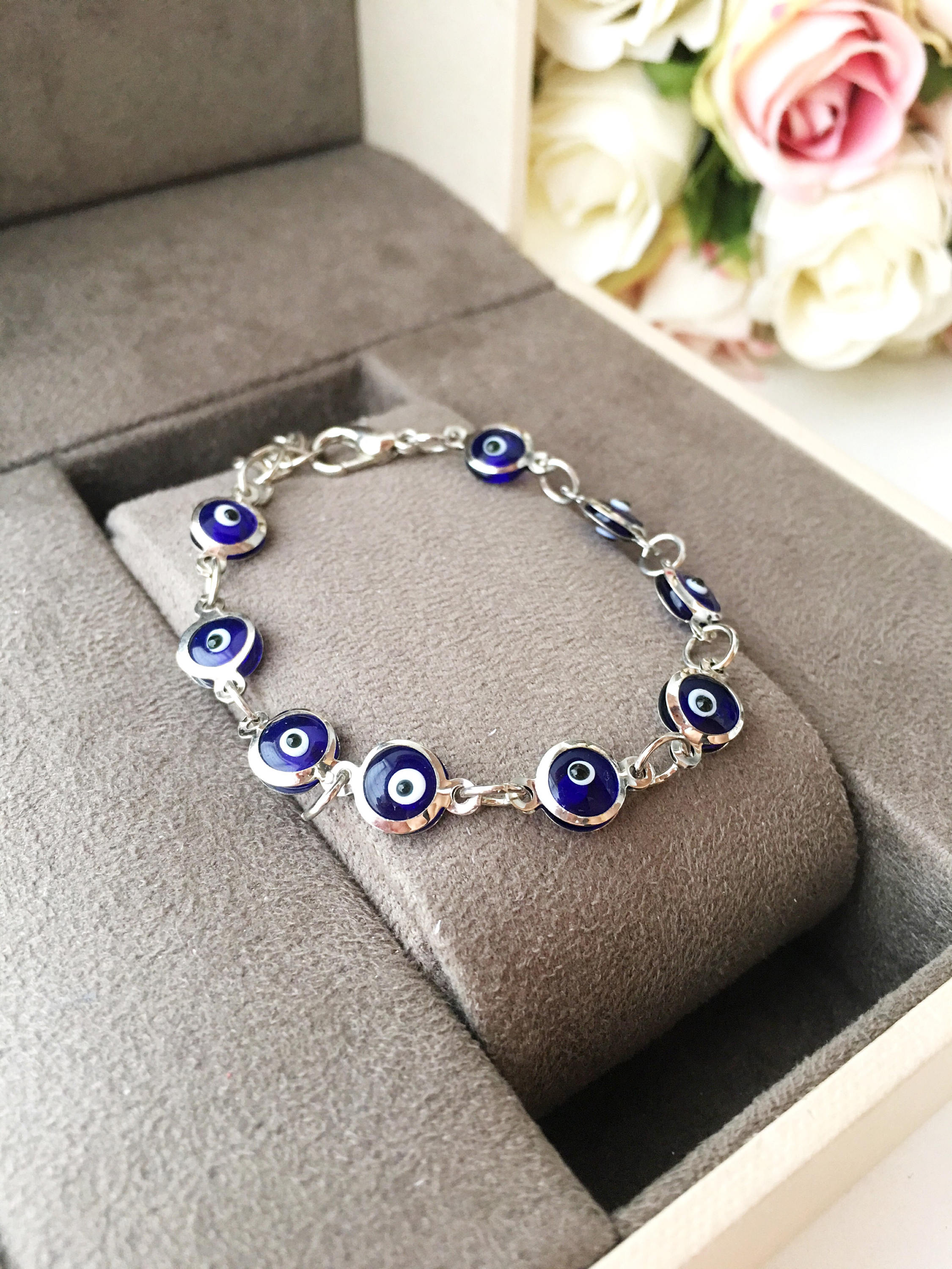 A beautiful silver chain bracelet featuring blue glass evil eye charms, showcasing handmade craftsmanship and elegant design.