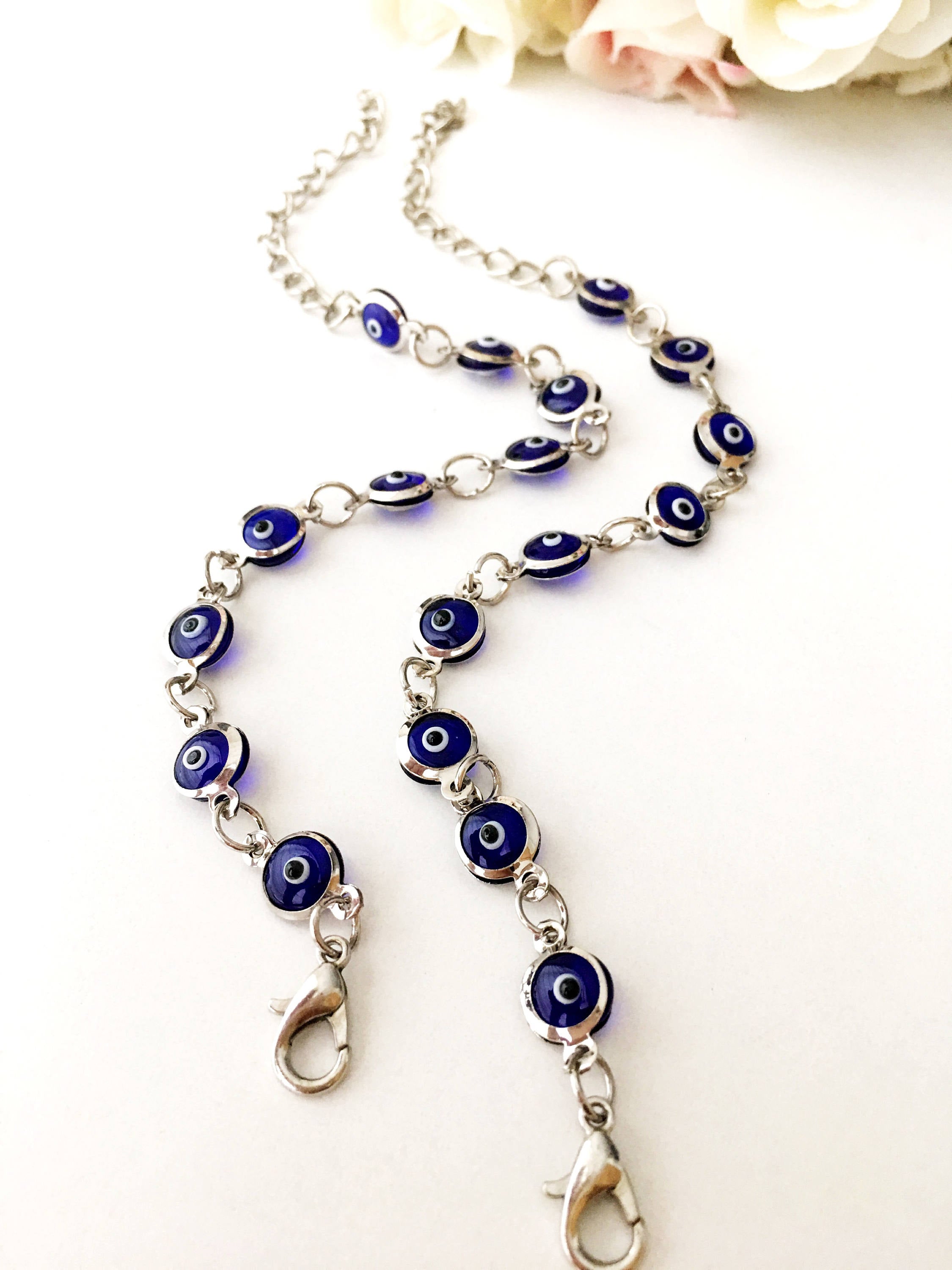 A beautiful silver chain bracelet featuring blue glass evil eye charms, showcasing handmade craftsmanship and elegant design.
