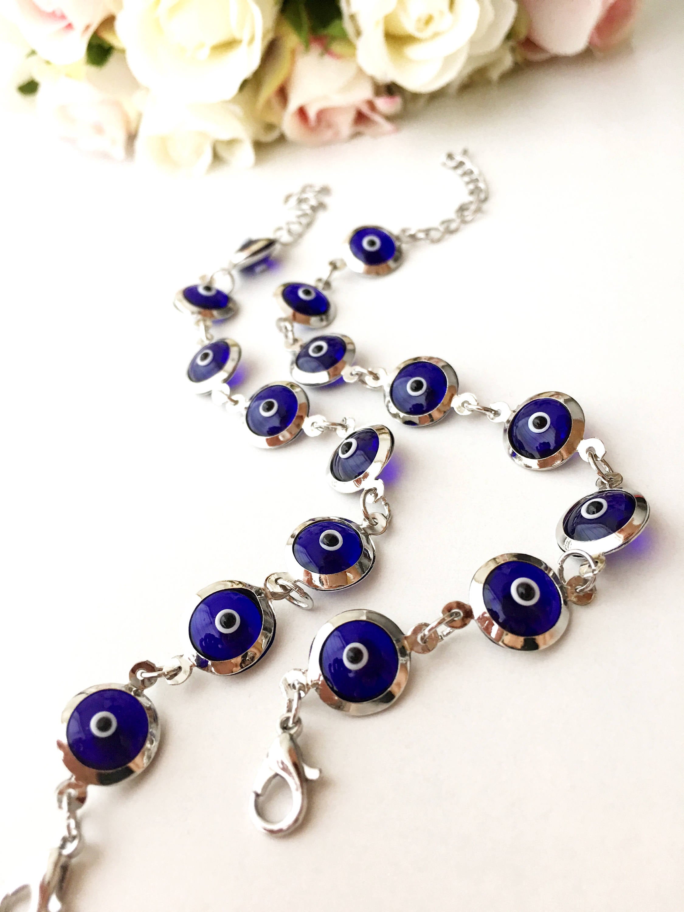A beautiful silver chain bracelet featuring blue glass evil eye charms, showcasing handmade craftsmanship and elegant design.