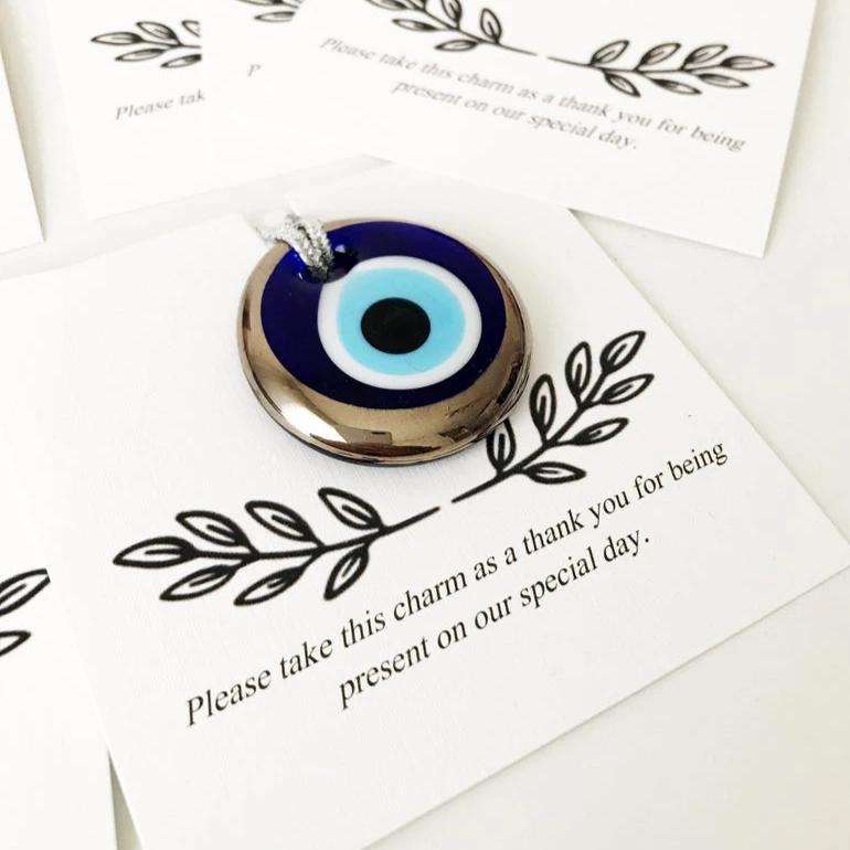 A collection of handmade silver evil eye beads with personalized cards, symbolizing good luck and protection, perfect for wedding favors.