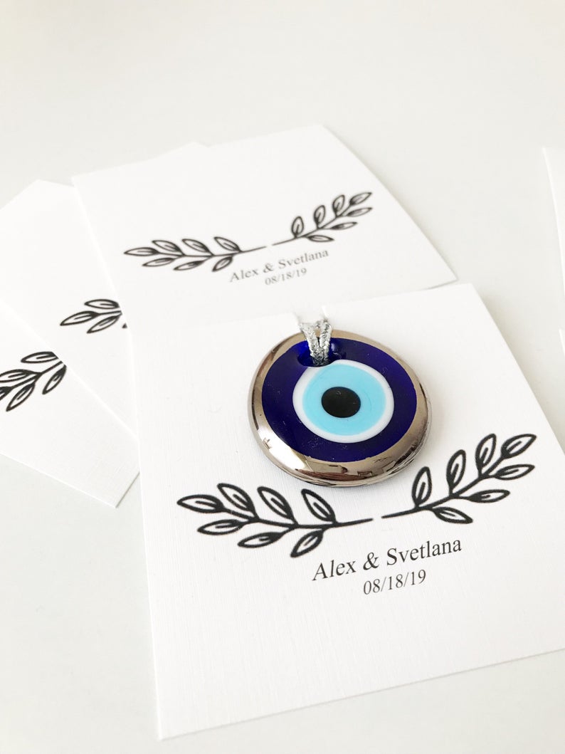 A collection of handmade silver evil eye beads with personalized cards, symbolizing good luck and protection, perfect for wedding favors.