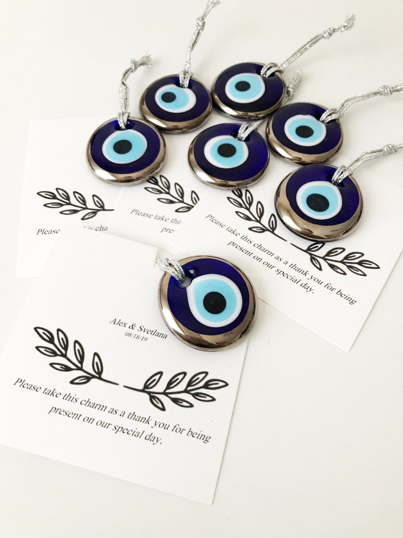 A collection of handmade silver evil eye beads with personalized cards, symbolizing good luck and protection, perfect for wedding favors.