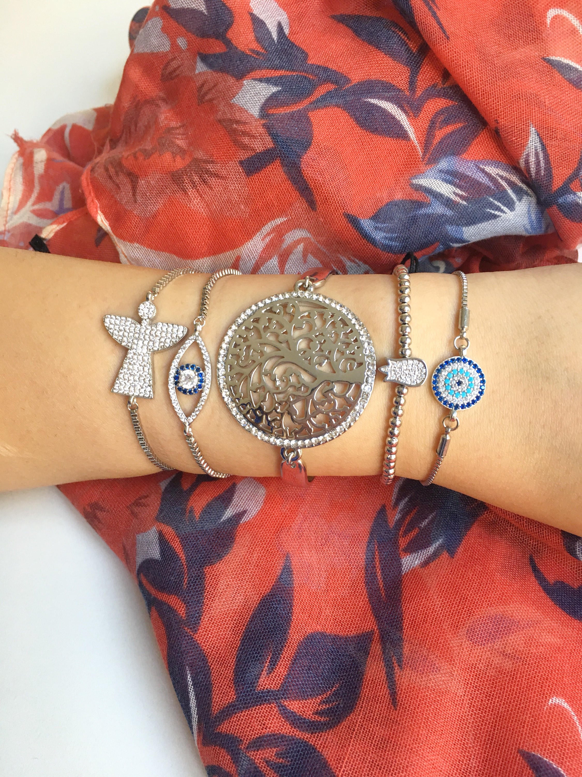 A beautiful set of handmade silver evil eye bracelets featuring various charms including tree of life, angel, and tulip designs, all adjustable for comfort.