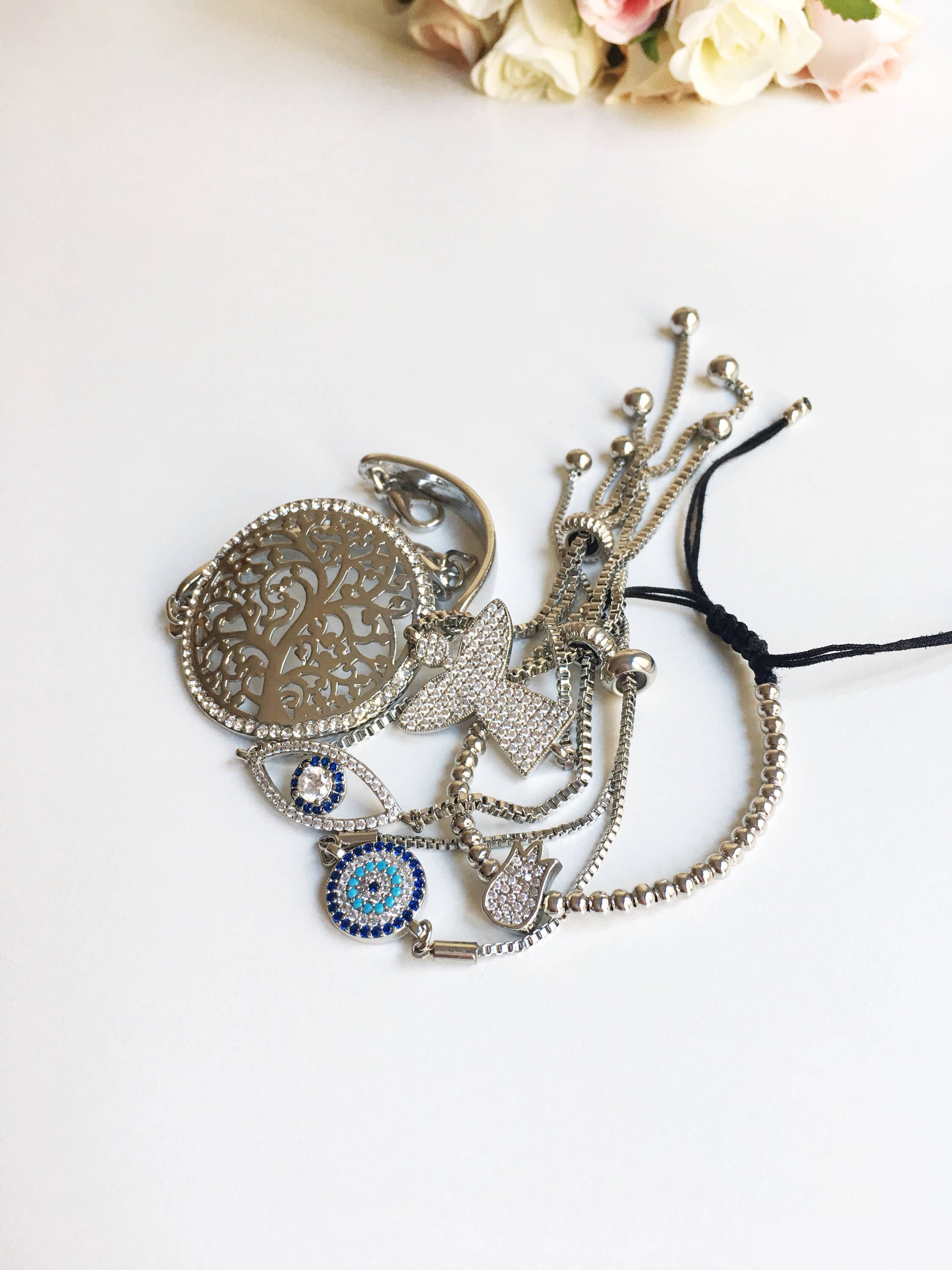 A beautiful set of handmade silver evil eye bracelets featuring various charms including tree of life, angel, and tulip designs, all adjustable for comfort.