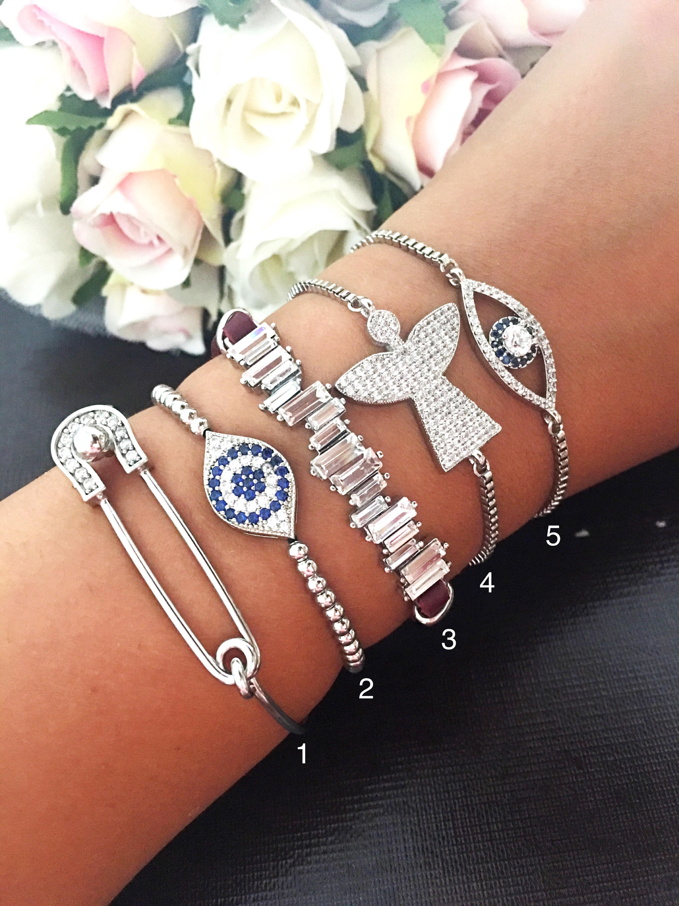 A beautiful set of handmade silver evil eye bracelets, featuring various designs including safety pin, baguette, and zirconia styles, all adjustable for comfort.