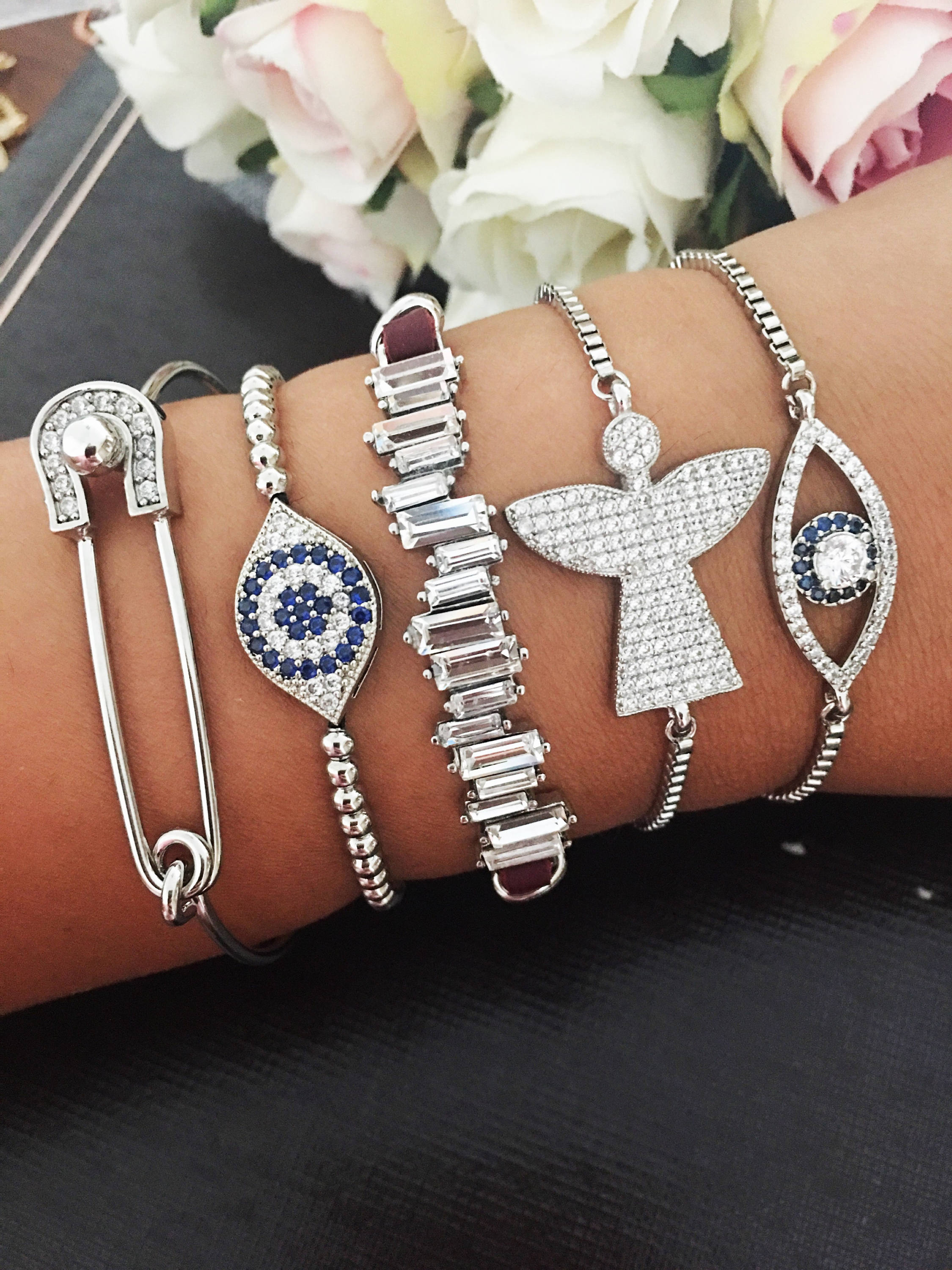 A beautiful set of handmade silver evil eye bracelets, featuring various designs including safety pin, baguette, and zirconia styles, all adjustable for comfort.