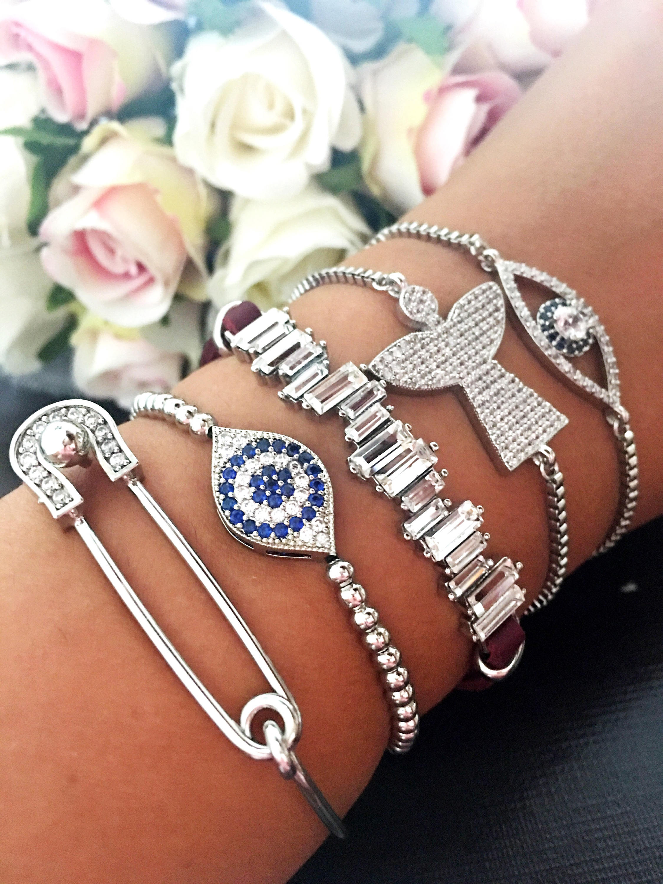 A beautiful set of handmade silver evil eye bracelets, featuring various designs including safety pin, baguette, and zirconia styles, all adjustable for comfort.