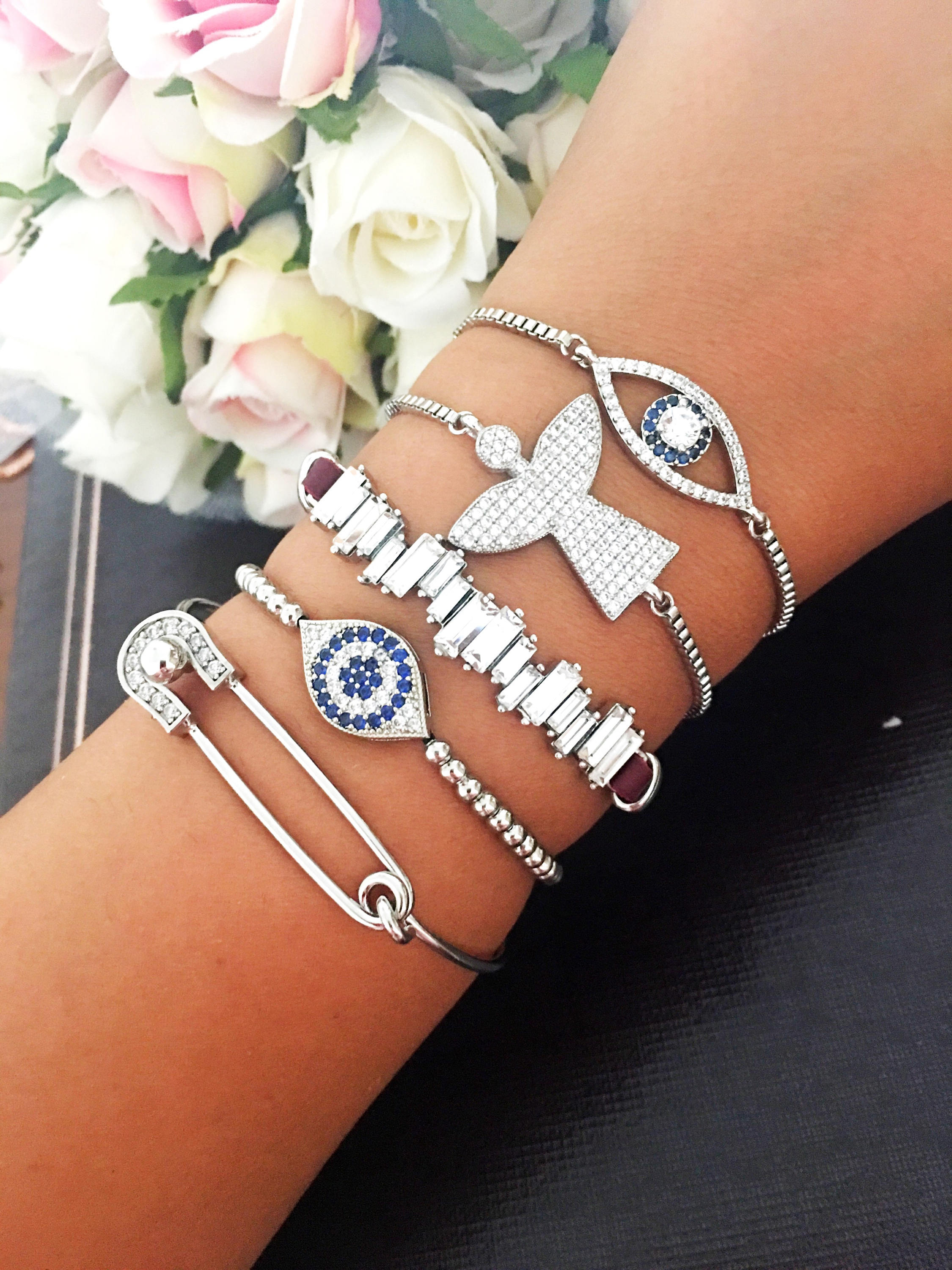 A beautiful set of handmade silver evil eye bracelets, featuring various designs including safety pin, baguette, and zirconia styles, all adjustable for comfort.