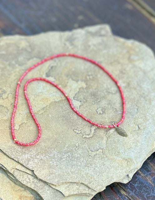 A stylish Speckled Red & Bronze Leaf Stretchy Seed Bead Pendant Necklace featuring reddish-orange Czech glass beads and a metallic silver starburst charm.