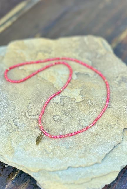 A stylish Speckled Red & Bronze Leaf Stretchy Seed Bead Pendant Necklace featuring reddish-orange Czech glass beads and a metallic silver starburst charm.