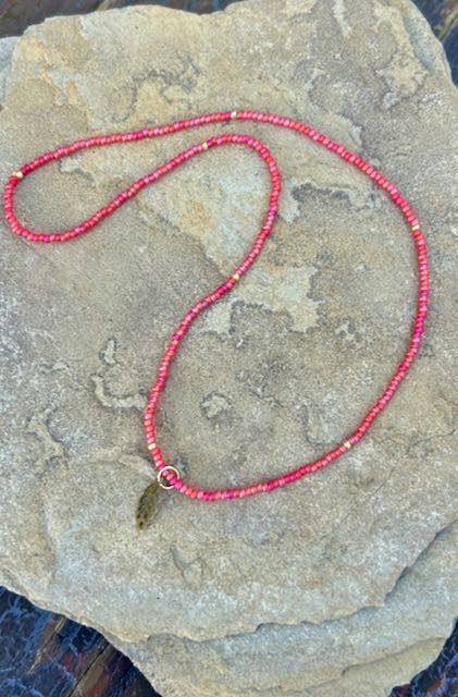 A stylish Speckled Red & Bronze Leaf Stretchy Seed Bead Pendant Necklace featuring reddish-orange Czech glass beads and a metallic silver starburst charm.
