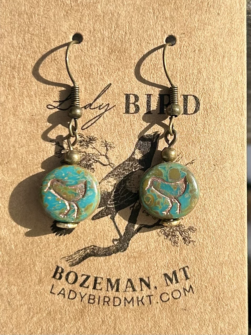 A pair of elegant earrings featuring speckled turquoise Czech glass beads and etched copper bird motifs, showcasing nature-inspired design.