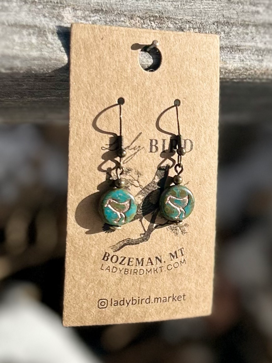 A pair of elegant earrings featuring speckled turquoise Czech glass beads and etched copper bird motifs, showcasing nature-inspired design.