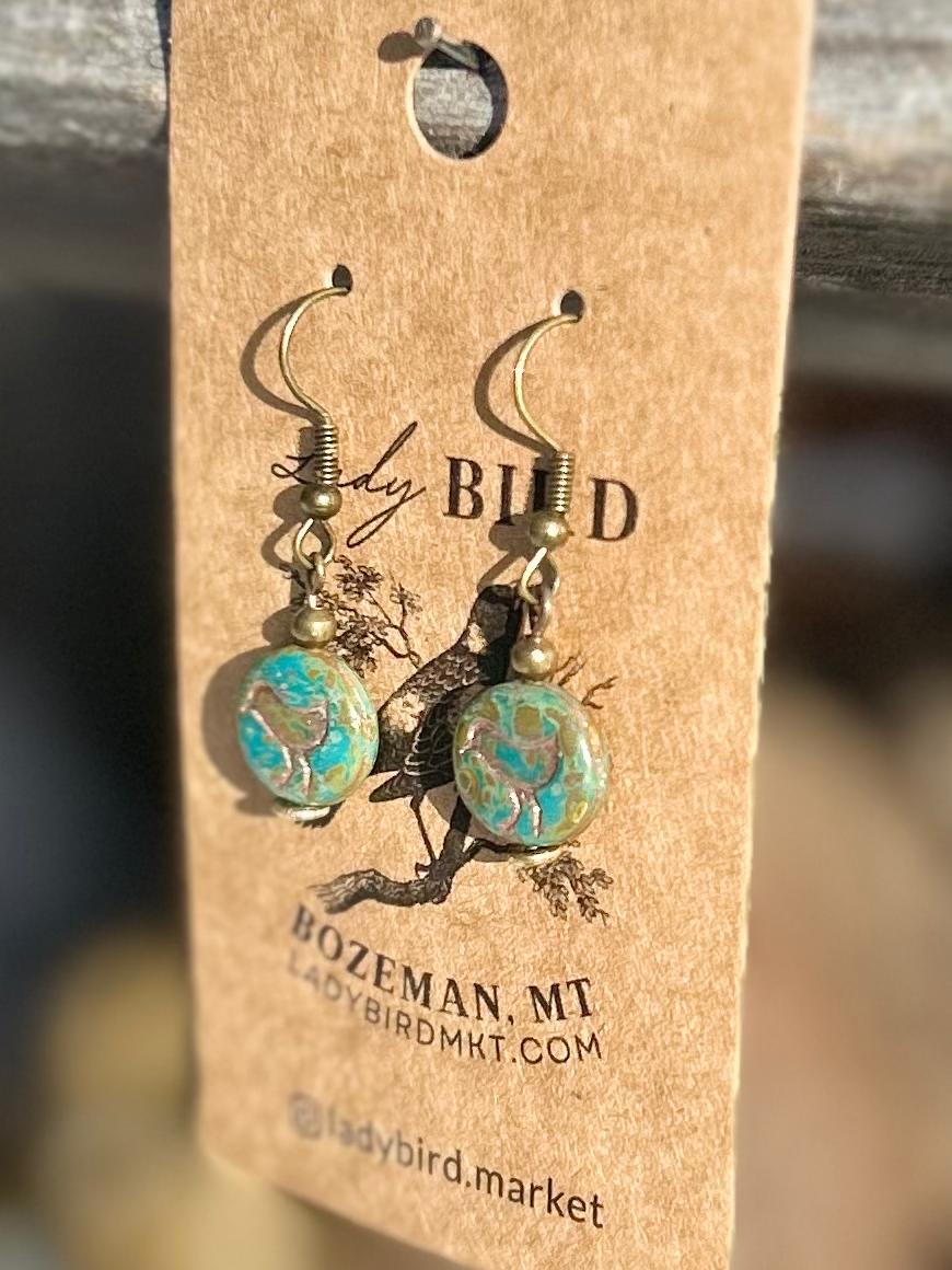 A pair of elegant earrings featuring speckled turquoise Czech glass beads and etched copper bird motifs, showcasing nature-inspired design.