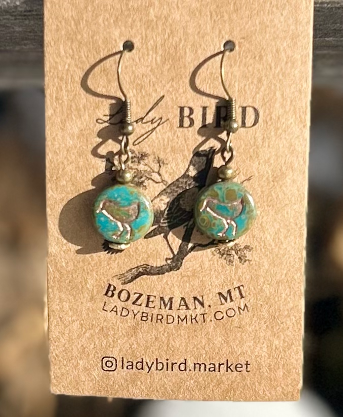 A pair of elegant earrings featuring speckled turquoise Czech glass beads and etched copper bird motifs, showcasing nature-inspired design.