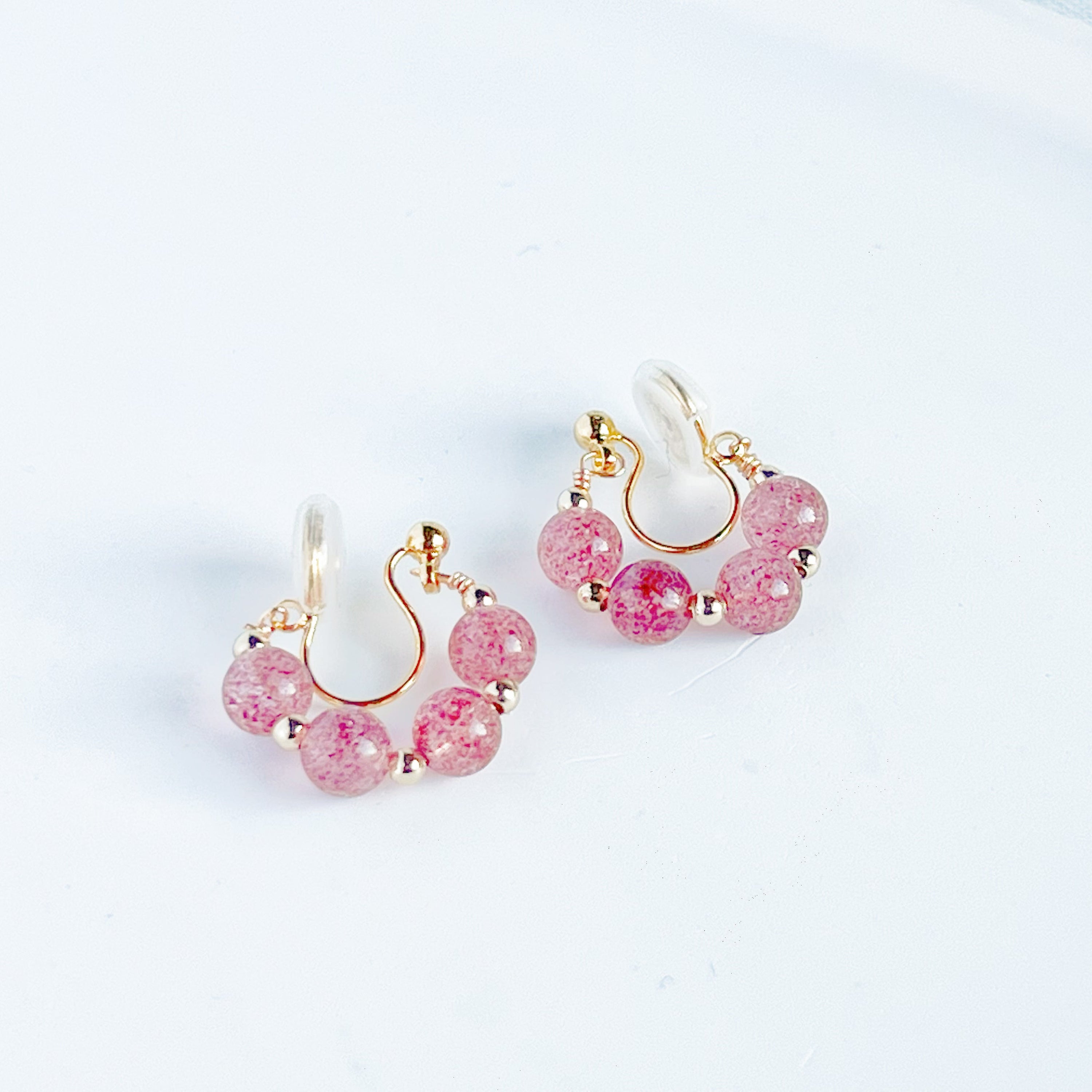 A pair of handmade hoop clip-on earrings featuring natural strawberry quartz beads, showcasing their vibrant pink hues and elegant design.