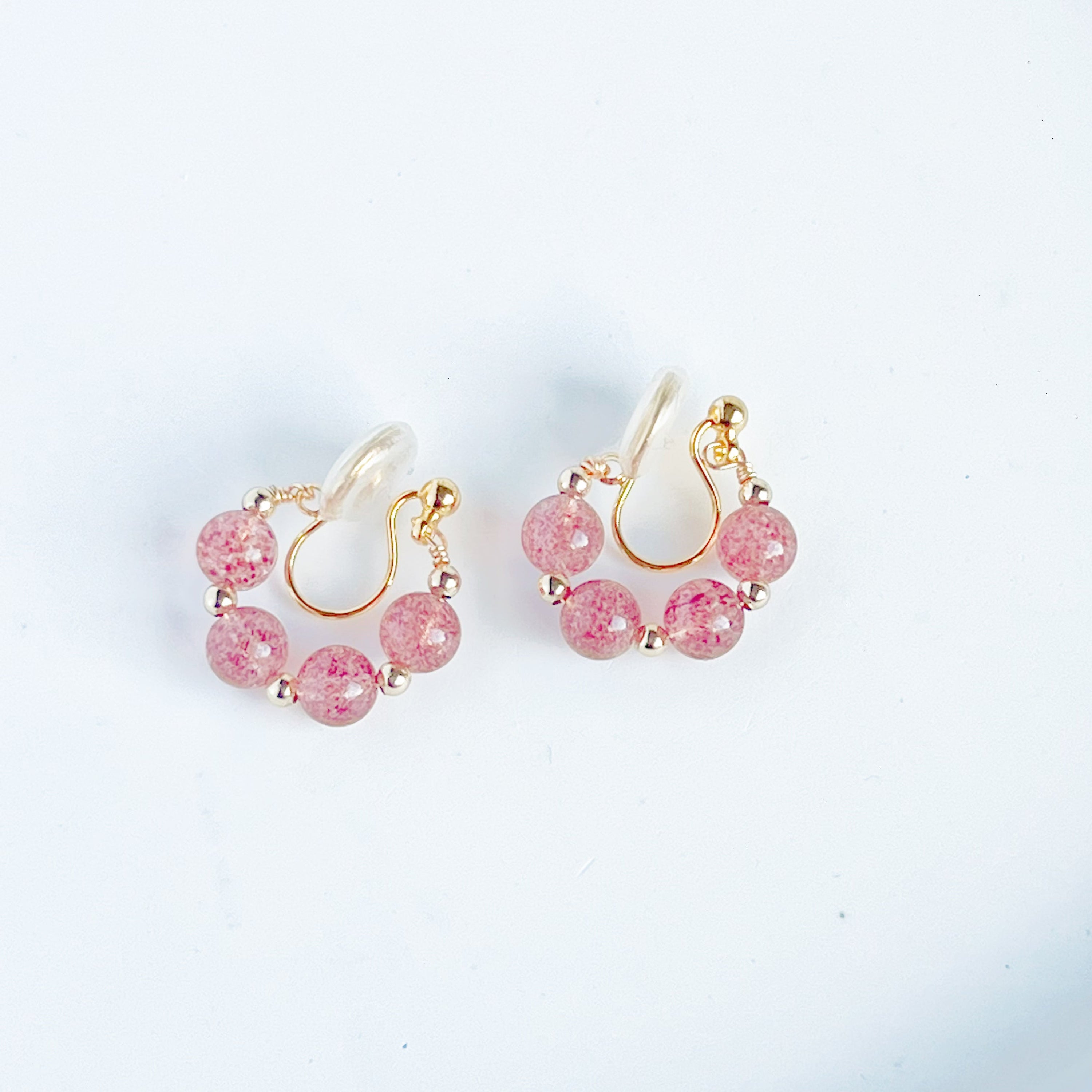 A pair of handmade hoop clip-on earrings featuring natural strawberry quartz beads, showcasing their vibrant pink hues and elegant design.