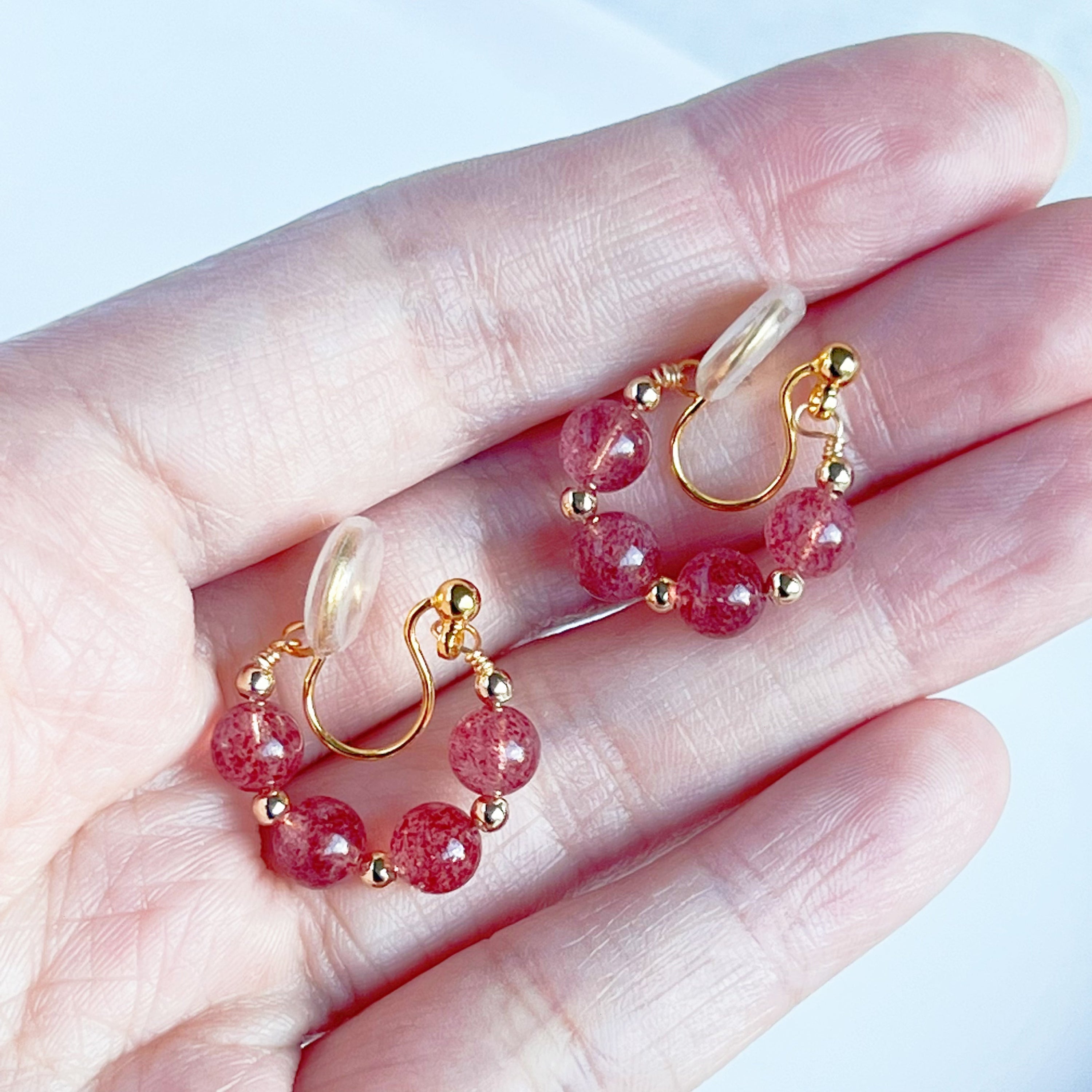 A pair of handmade hoop clip-on earrings featuring natural strawberry quartz beads, showcasing their vibrant pink hues and elegant design.