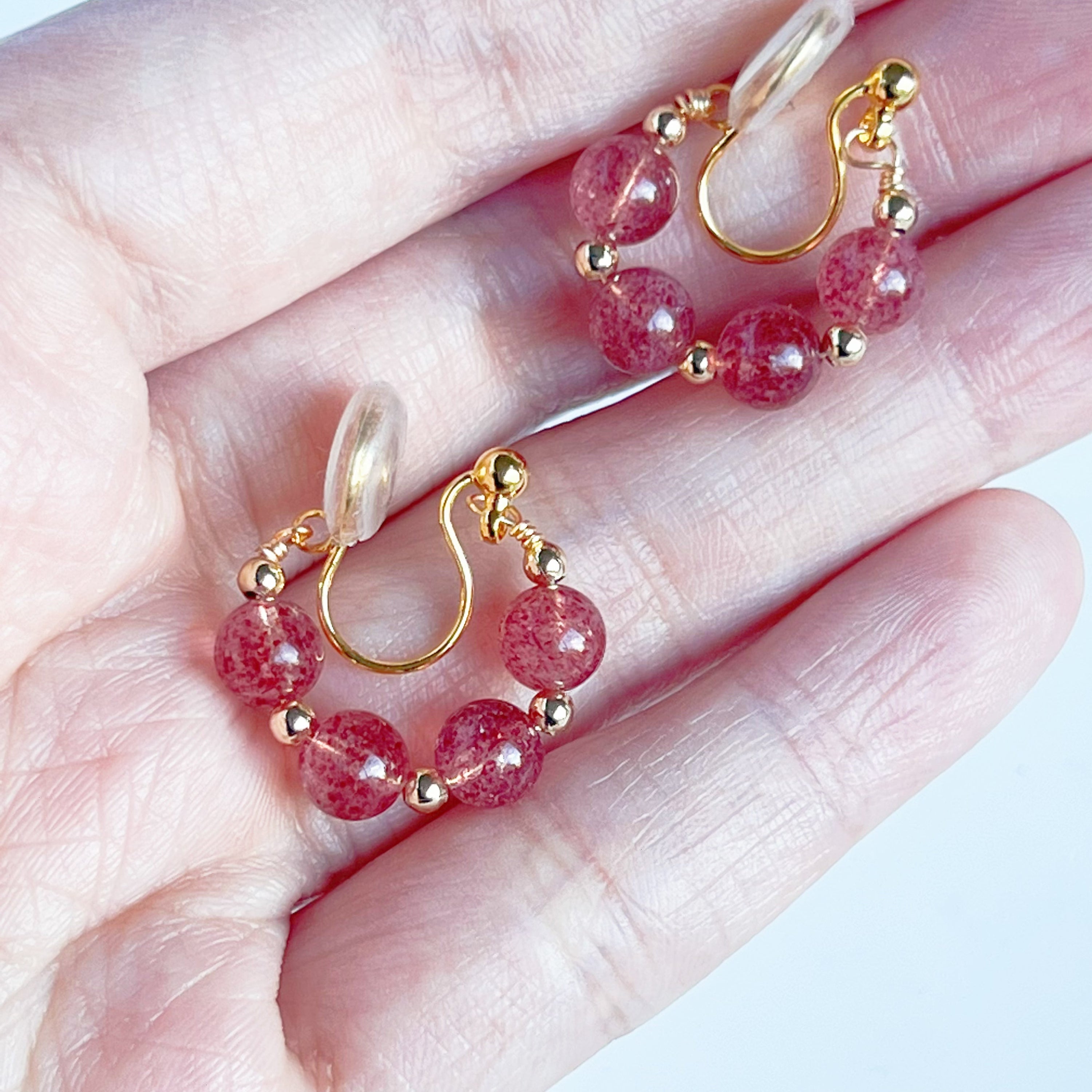A pair of handmade hoop clip-on earrings featuring natural strawberry quartz beads, showcasing their vibrant pink hues and elegant design.