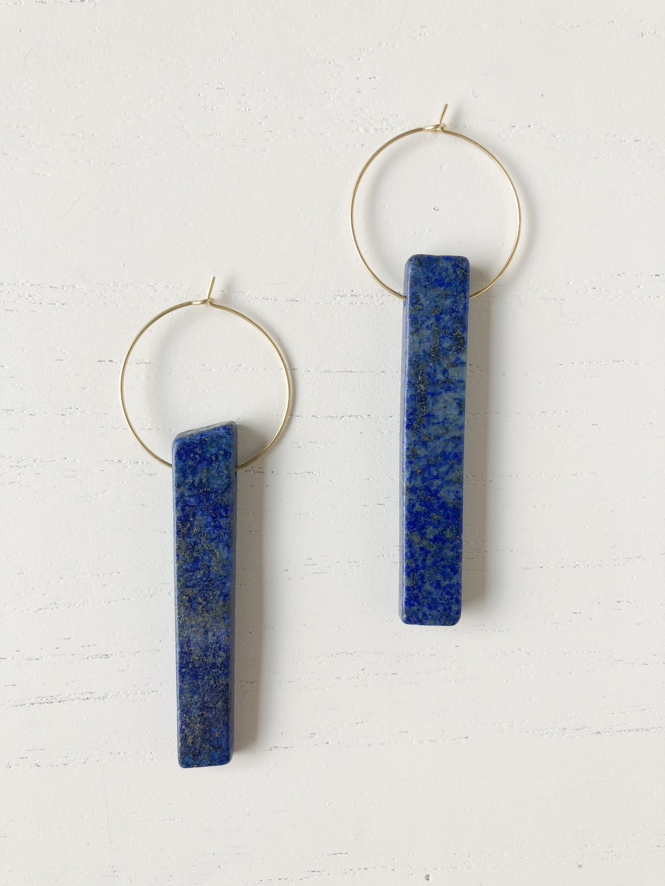 The Henley Lapis earrings featuring a brass hoop and a vibrant lapis stone, showcasing their unique design and color.