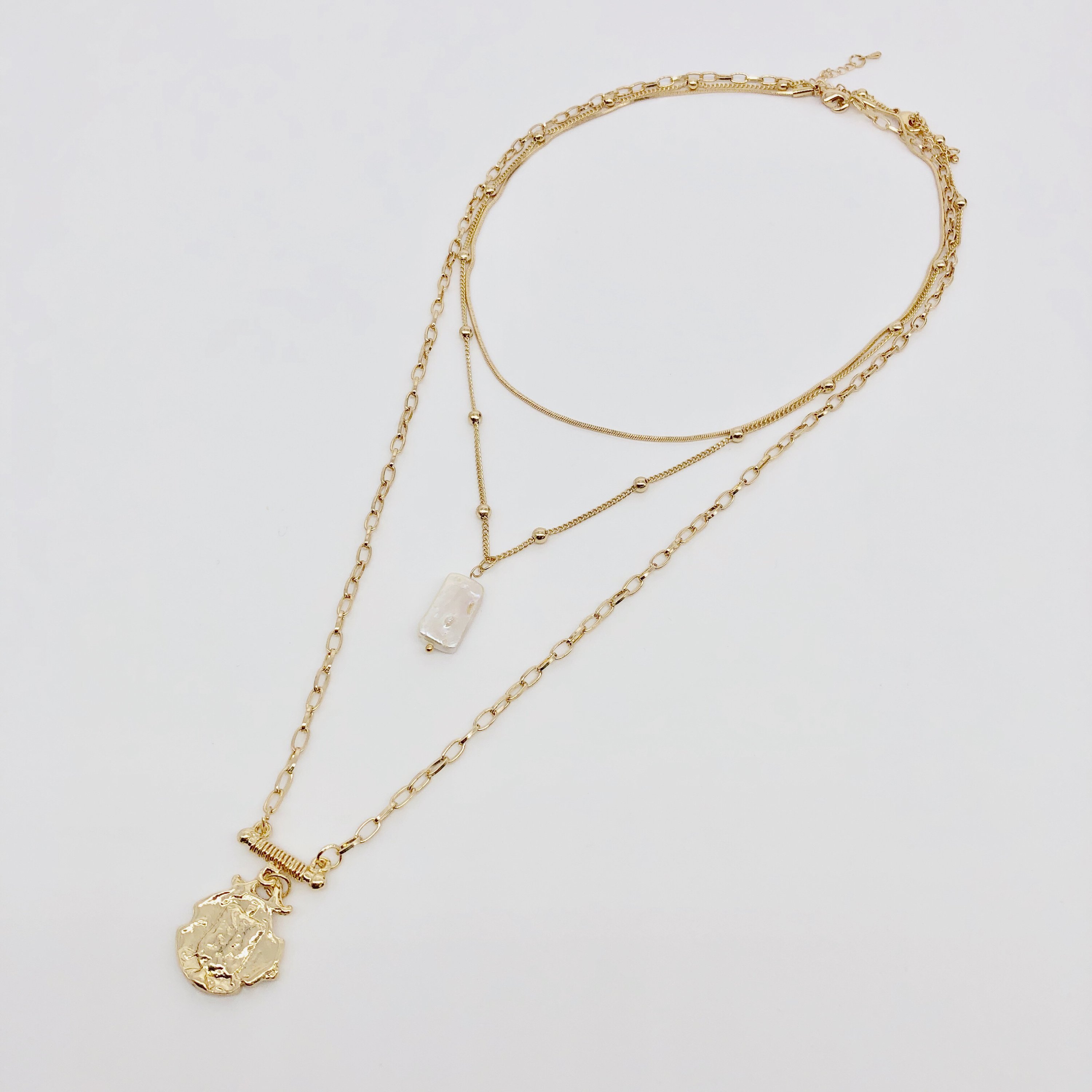Three layer necklace featuring simulated pearl and gold pendant, elegantly designed with textured links and beaded accents.