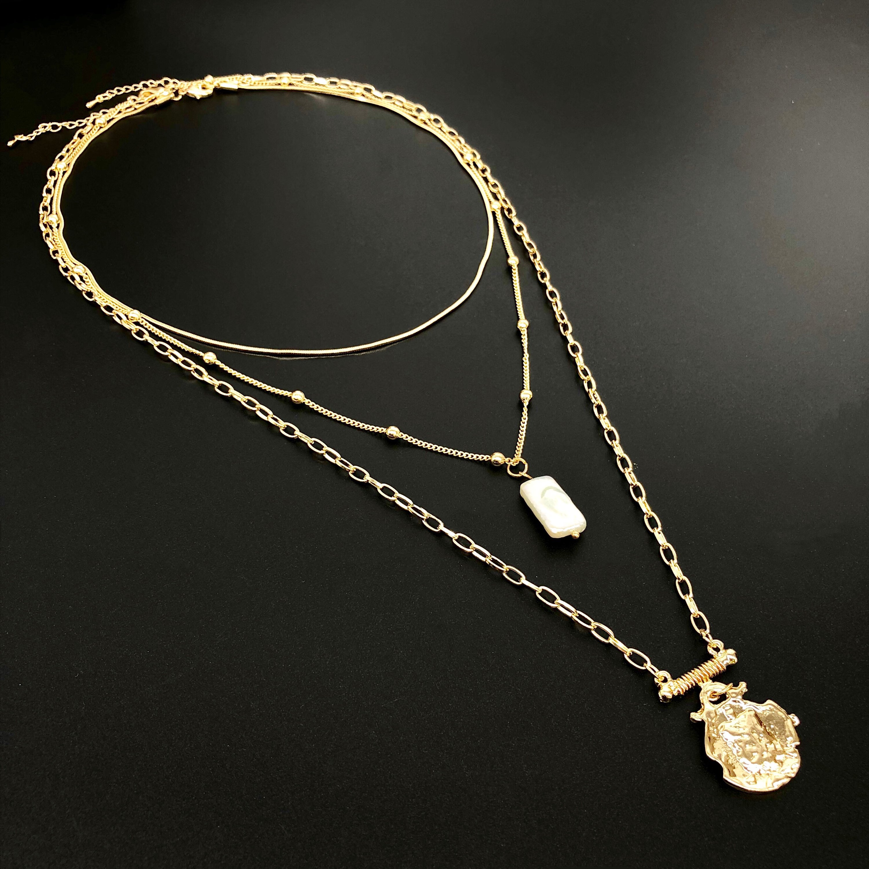 Three layer necklace featuring simulated pearl and gold pendant, elegantly designed with textured links and beaded accents.