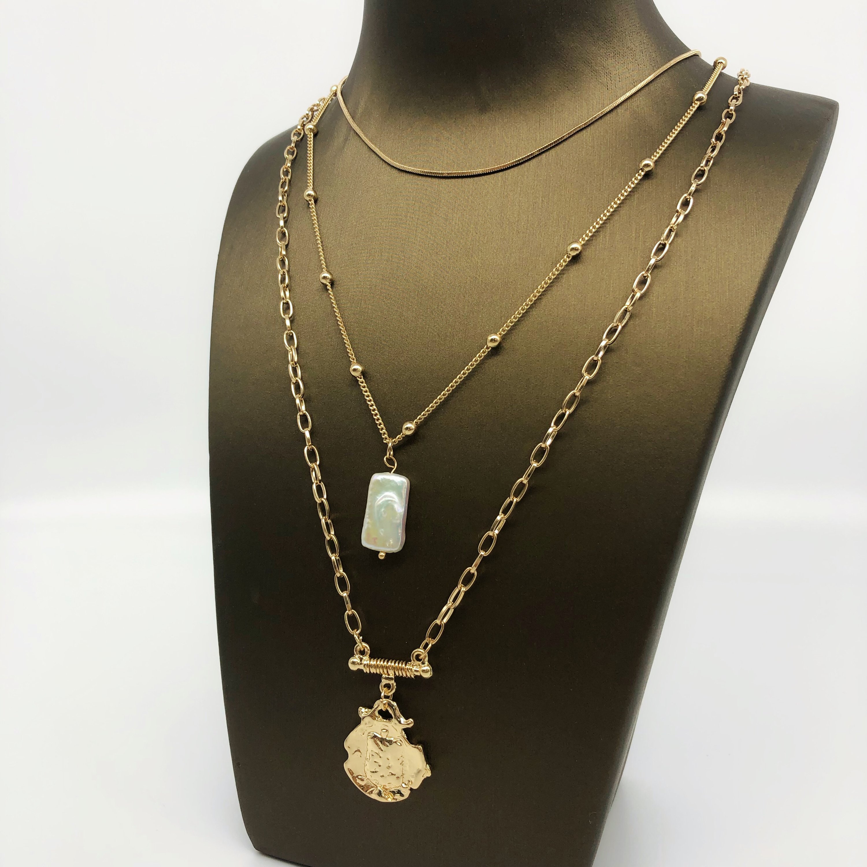 Three layer necklace featuring simulated pearl and gold pendant, elegantly designed with textured links and beaded accents.