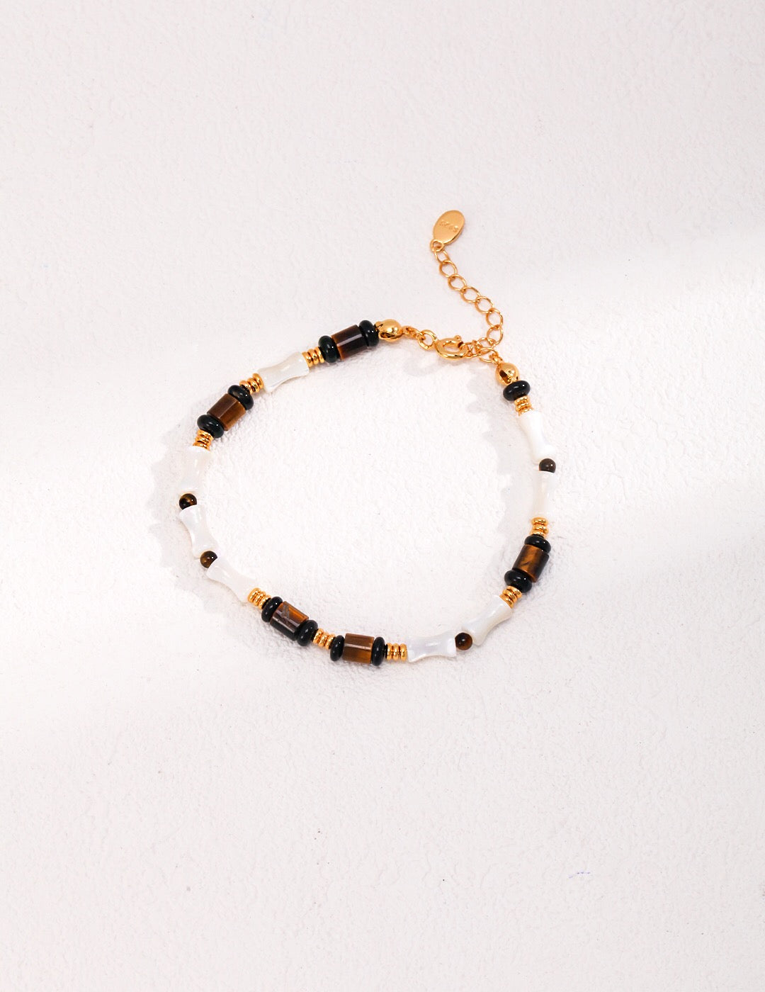 A beautifully handcrafted bracelet featuring tiger eye stones, mother shell, and black agate, with a gold vermeil chain.