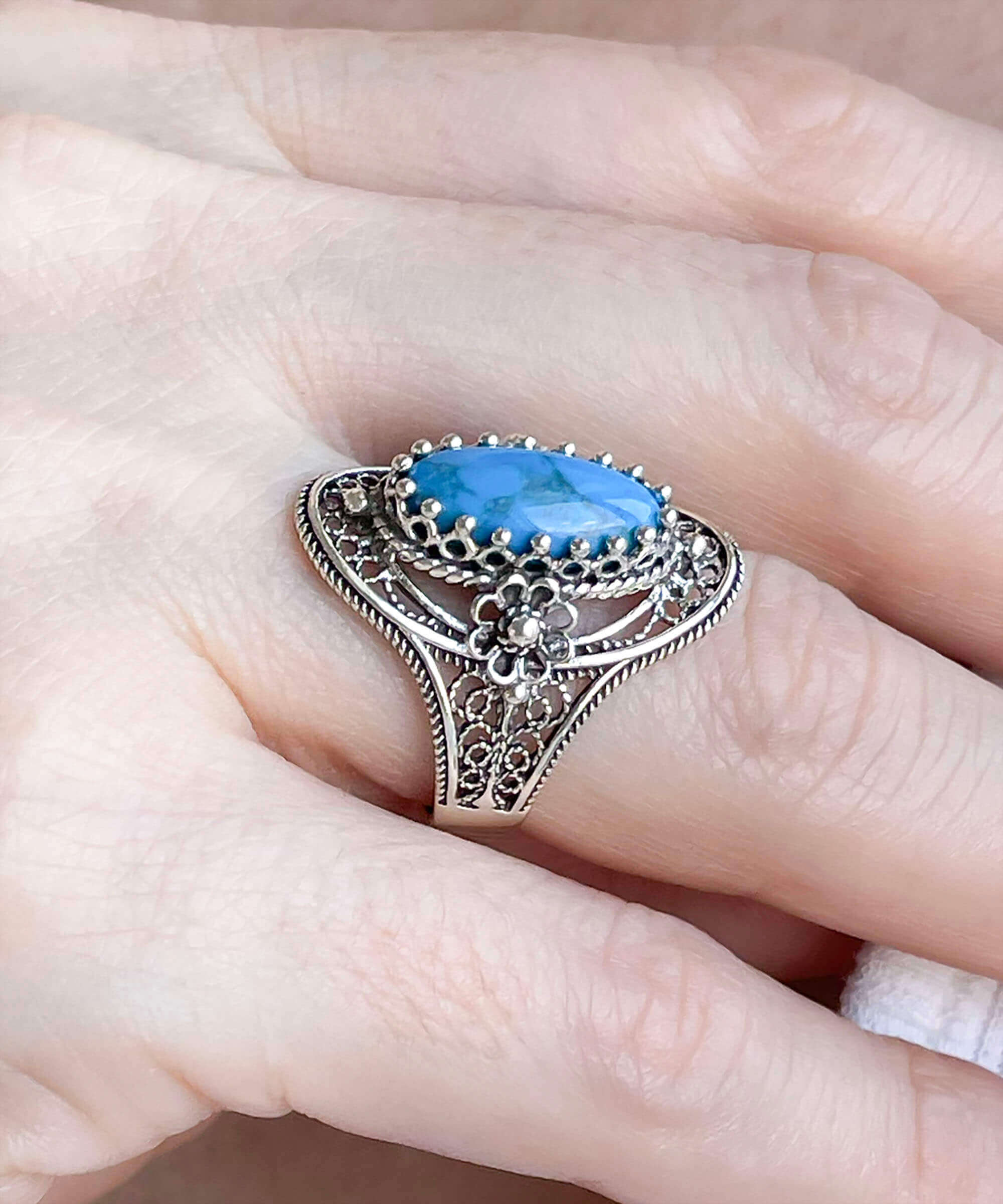 Turquoise gemstone sterling silver filigree ring with daisy accents, showcasing an oval cut turquoise stone and intricate design.