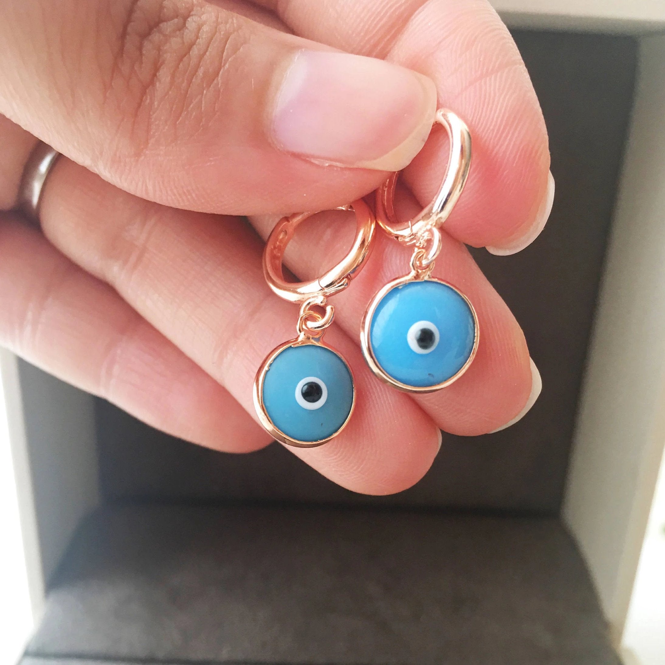 A pair of handmade turquoise hoop earrings featuring a glass evil eye bead, showcasing intricate craftsmanship and vibrant colors.