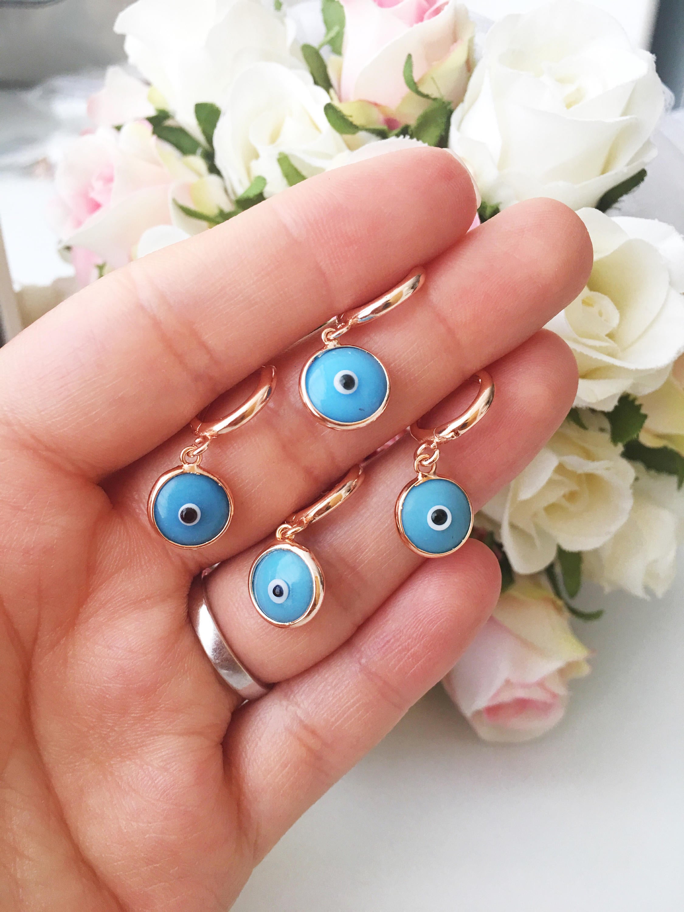 A pair of handmade turquoise hoop earrings featuring a glass evil eye bead, showcasing intricate craftsmanship and vibrant colors.