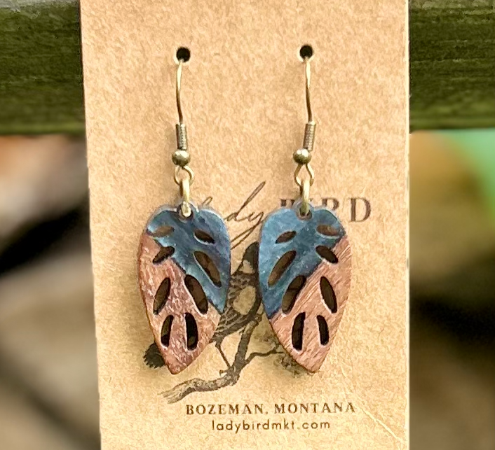 A pair of leaf-shaped earrings made from walnut wood and black resin, showcasing unique wood grain patterns and a lightweight design.