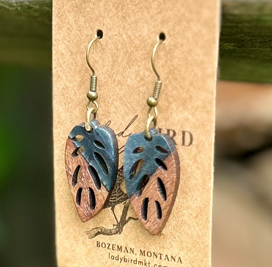 A pair of leaf-shaped earrings made from walnut wood and black resin, showcasing unique wood grain patterns and a lightweight design.