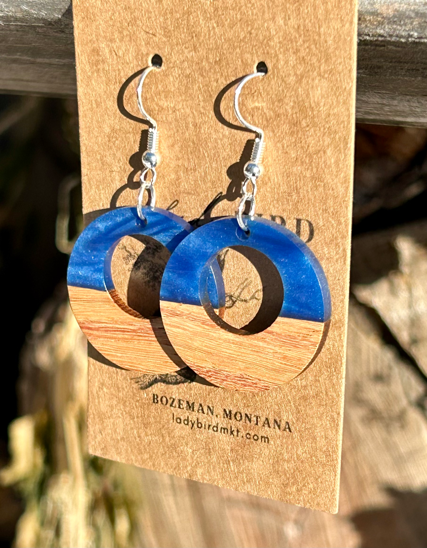 A pair of circle hoop earrings made from walnut wood and pearly blue resin, showcasing unique wood grain and vibrant color.