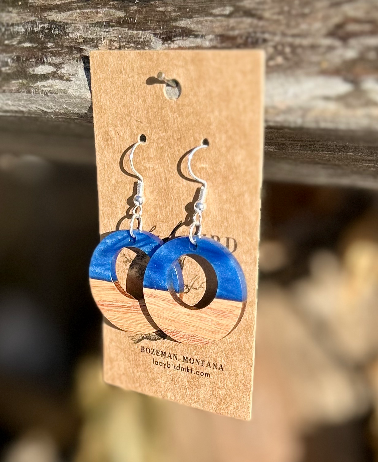 A pair of circle hoop earrings made from walnut wood and pearly blue resin, showcasing unique wood grain and vibrant color.