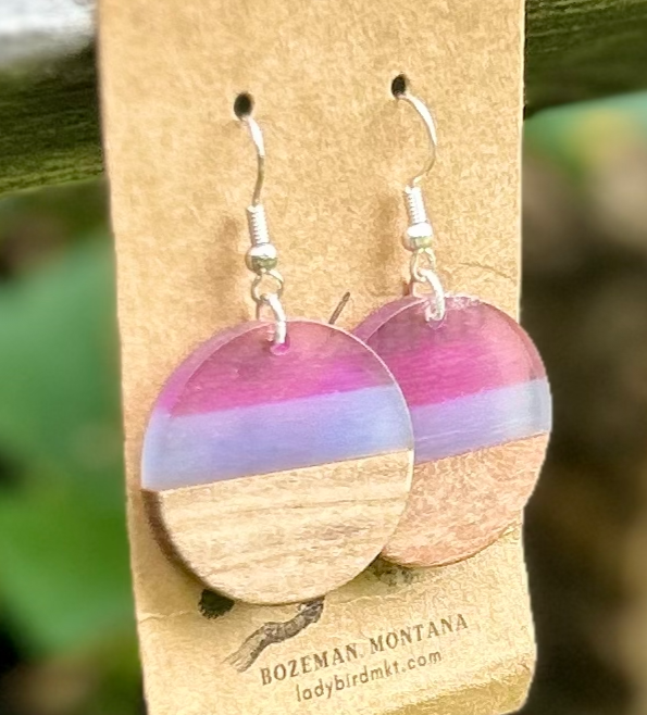 A pair of circle earrings made from walnut wood and purple resin, showcasing unique grain patterns and vibrant colors.