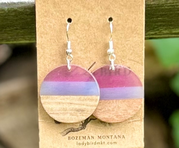 A pair of circle earrings made from walnut wood and purple resin, showcasing unique grain patterns and vibrant colors.