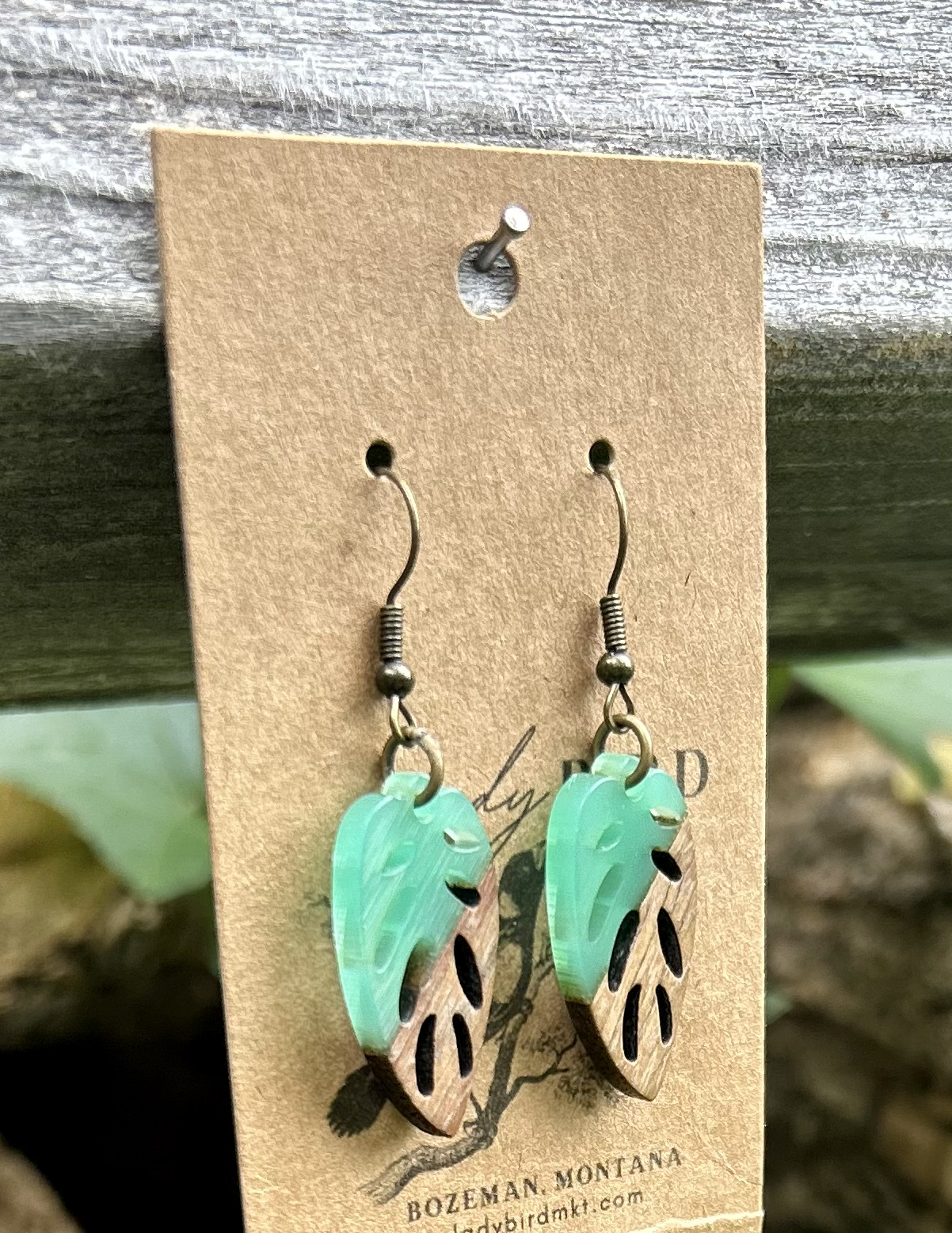 A pair of leaf-shaped earrings made from walnut wood and translucent turquoise resin, showcasing unique wood grain patterns.