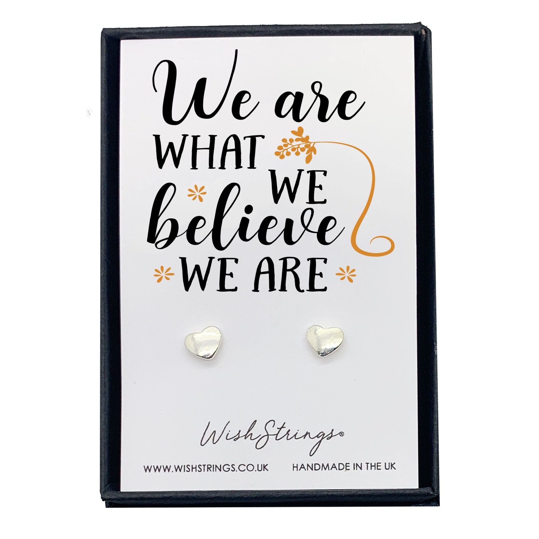 A pair of WE ARE WHAT WE BELIEVE earrings displayed in a black gift box with an inspirational card.