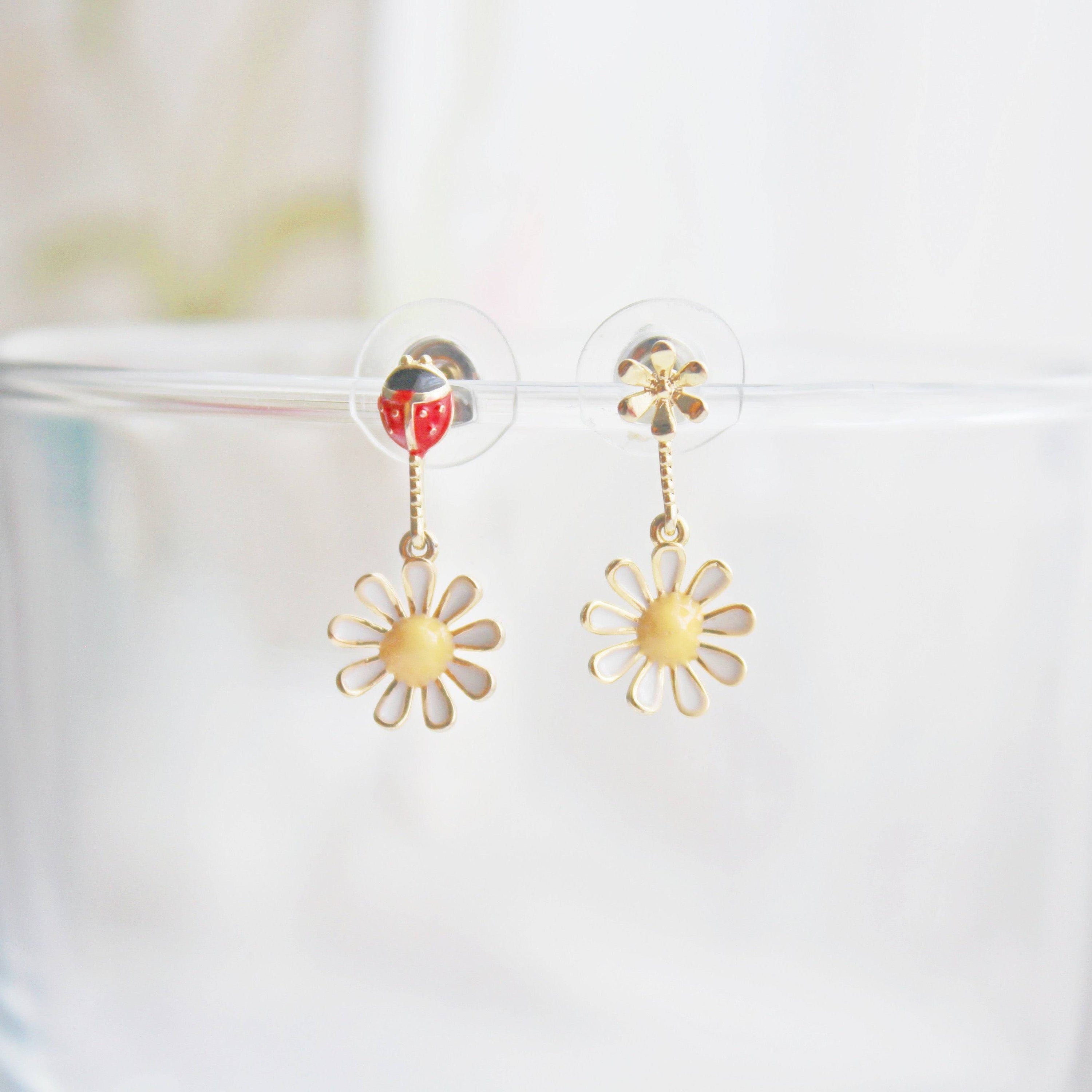 A pair of White Daisy Flower and Ladybird Mini Drop Mismatch Earrings featuring sterling silver ear studs and gold-coated bronze bodies.